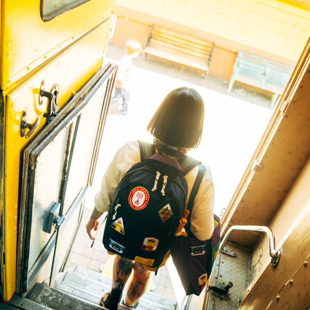 A person with a backpack exiting a train. Bright light in the background.
