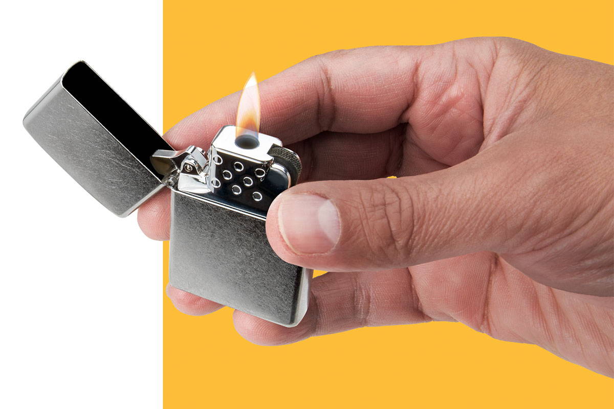Handing holding chrome lighter with a yellow flame butane insert.