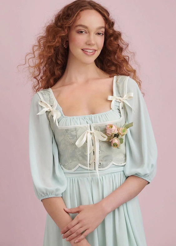 Smiling woman in a pastel blue dress with floral accents.