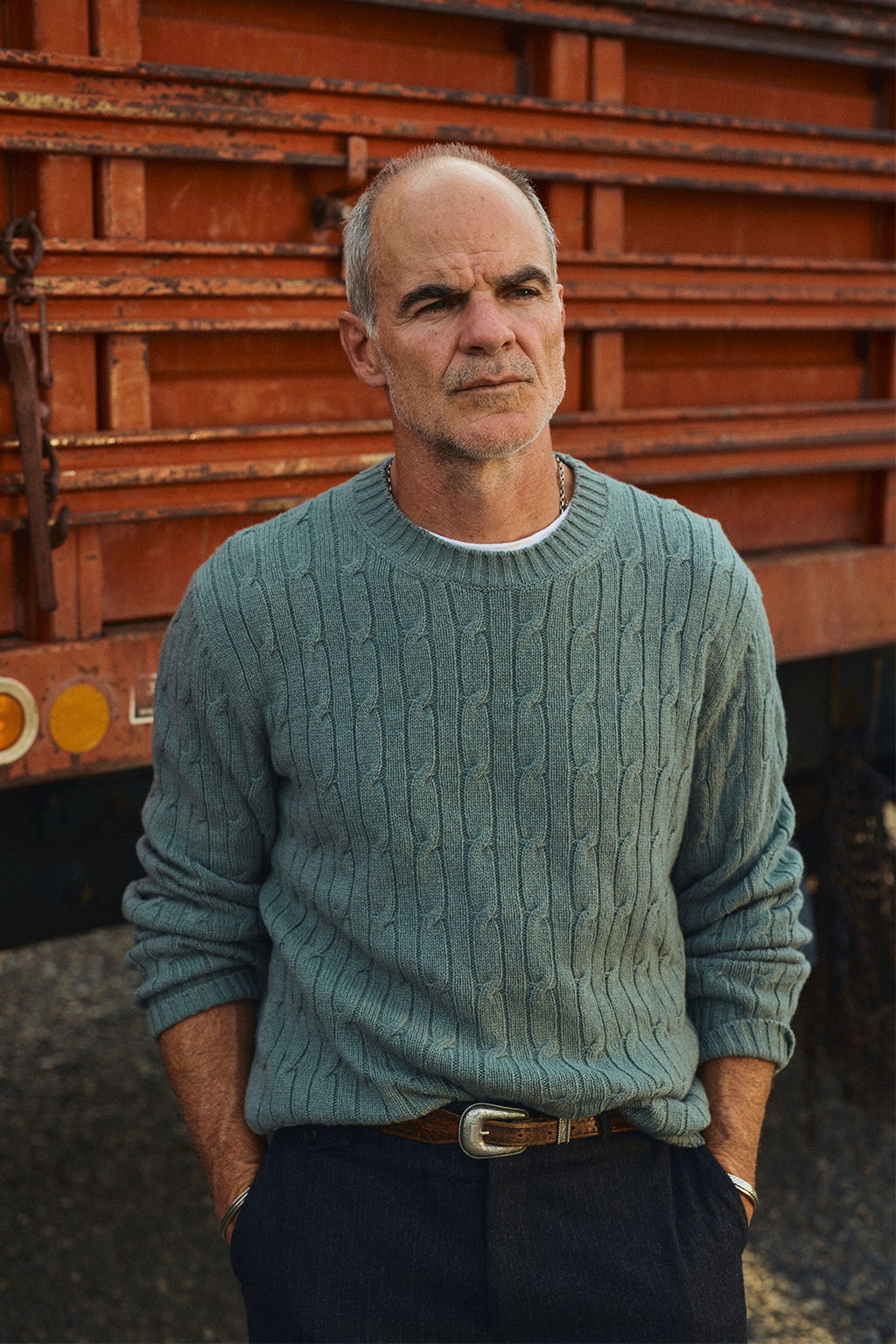 Micahel Kelly in a Livingston, Montana service station wearing the Bowen Cashmere Cable Sweater in Stone Green and the Rivay Italian Wool Suit in Charcoal Herringbone Trousers