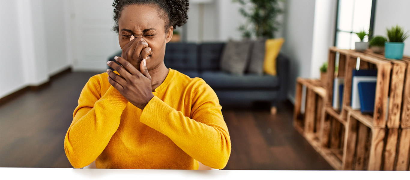 Young African American woman wearing casual clothes sitting on the table at home smelling vinegar smell from air conditioner holding her breath with fingers on her nose