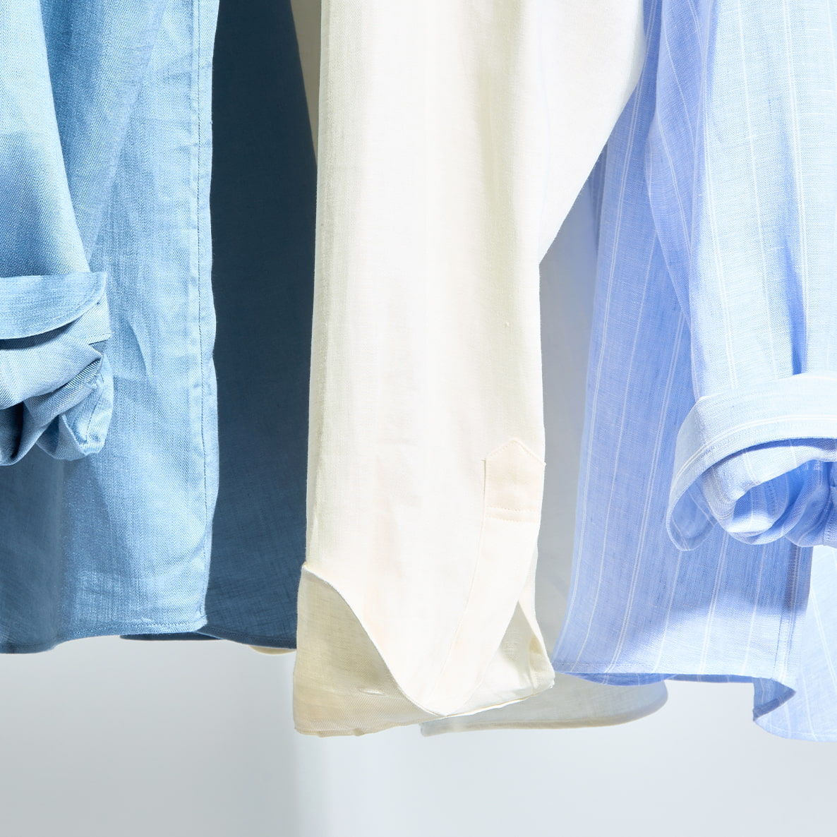 Three shirts hanging, light blue, cream, and light blue fabric.