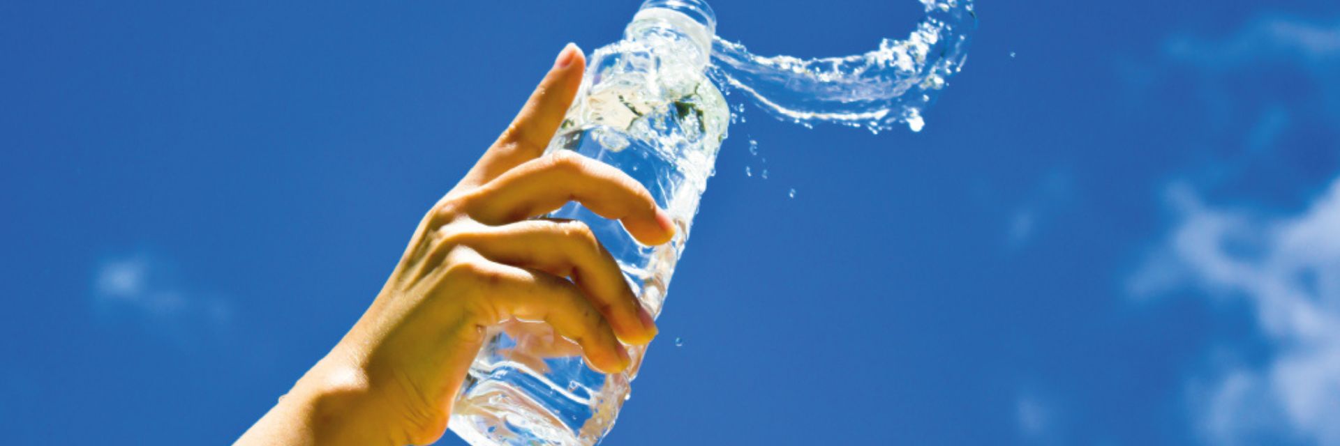 Hand holding a water bottle with splashes against a blue sky.