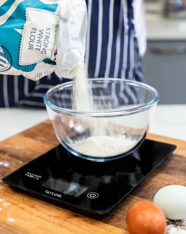 A bowl on kitchen scales with flour being poured into it.