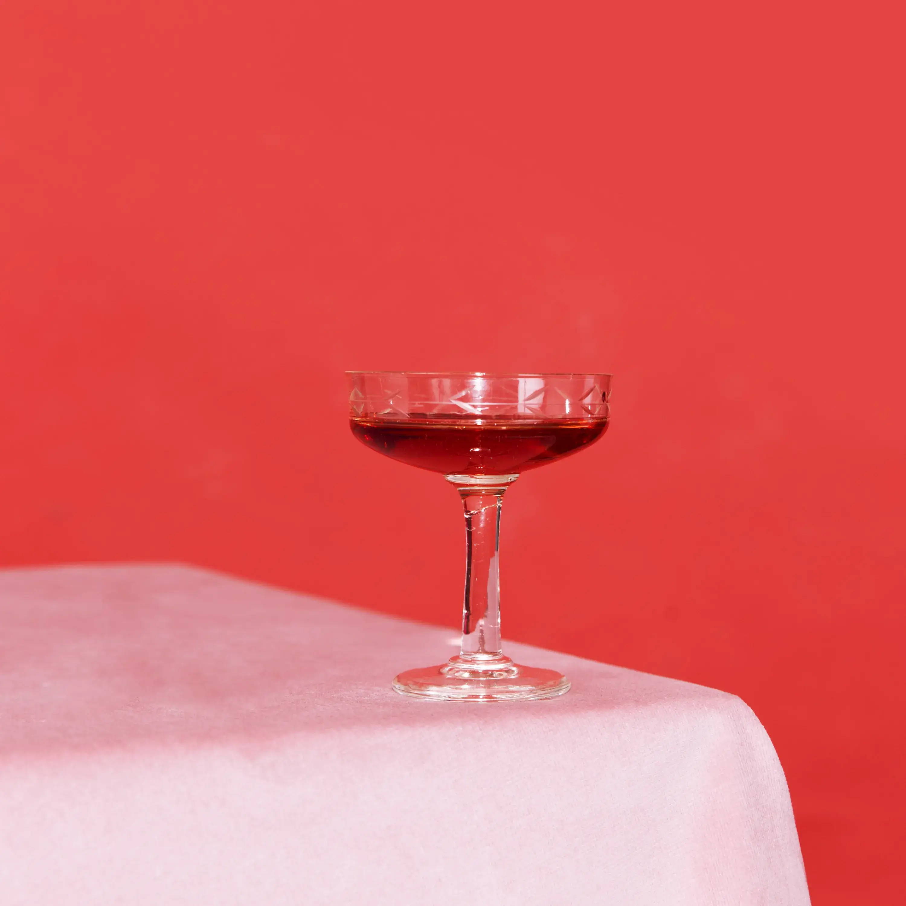 Taça de martini no canto de uma mesa com líquido vermelho dentro