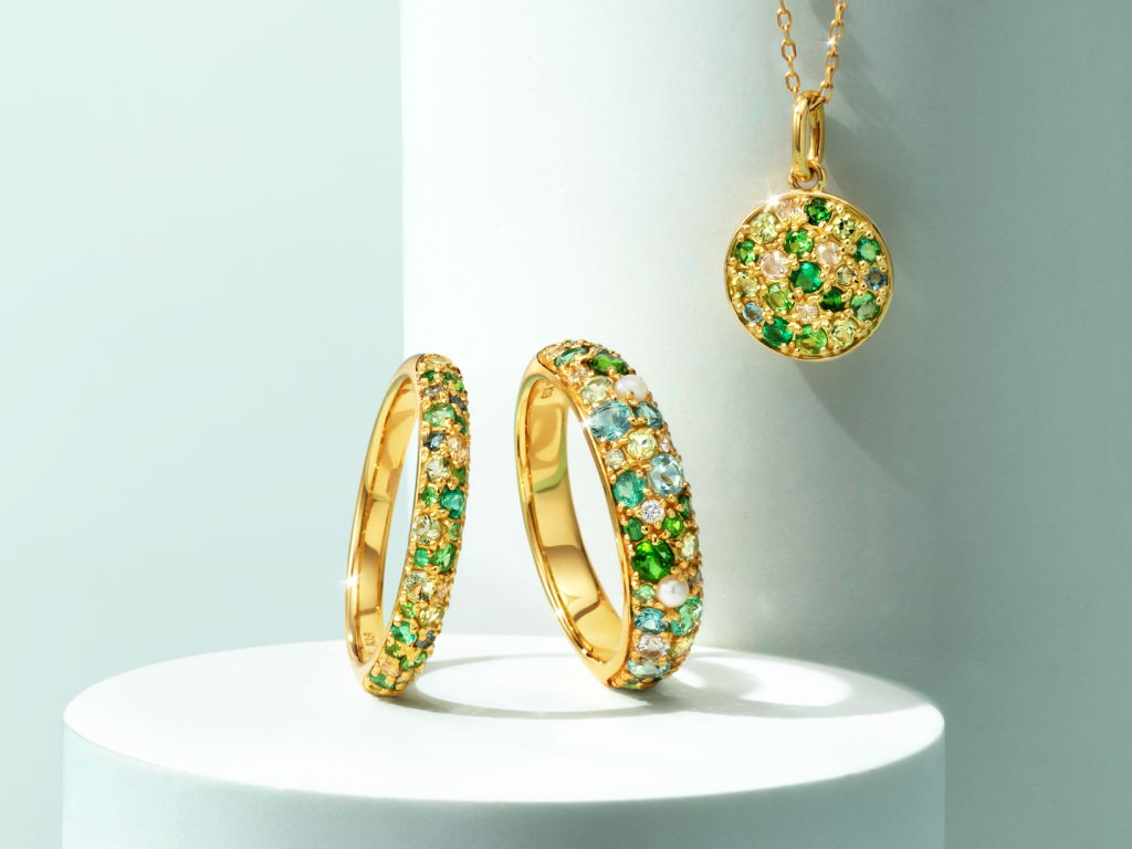 Gold jewelry with green and blue accents displayed on a white pedestal.