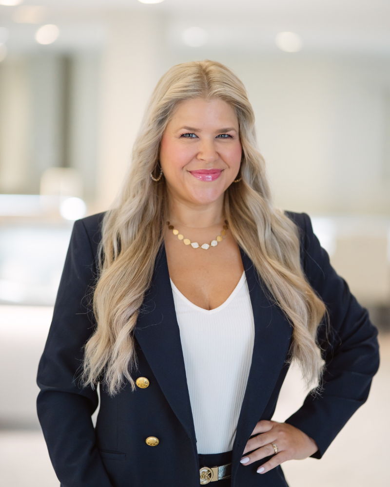 Professional woman in a blazer smiling in a bright, modern setting.
