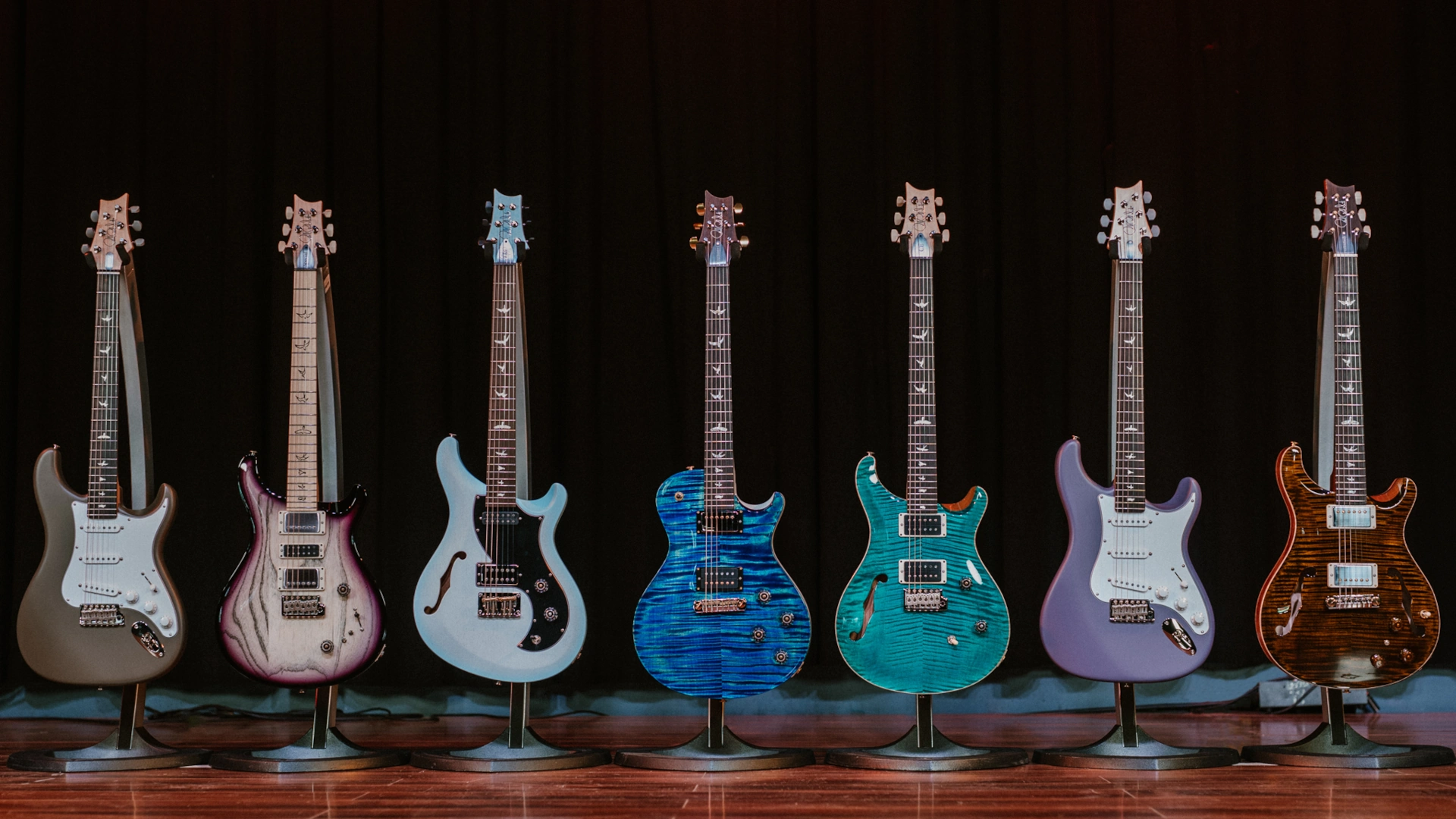 Eight PRS guitars displayed on stands against a dark background.
