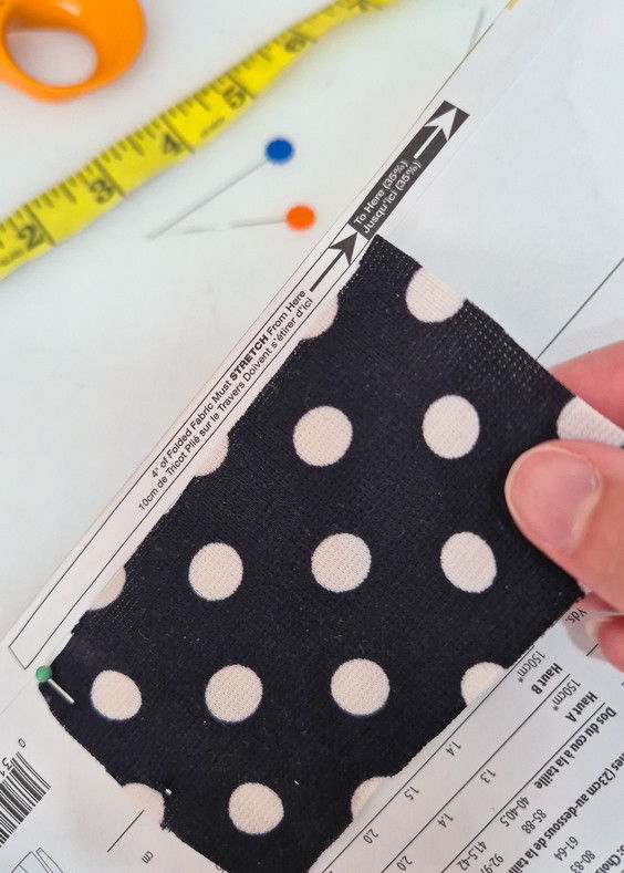Hand holding polka dot fabric swatch over sewing pattern and measuring tape.