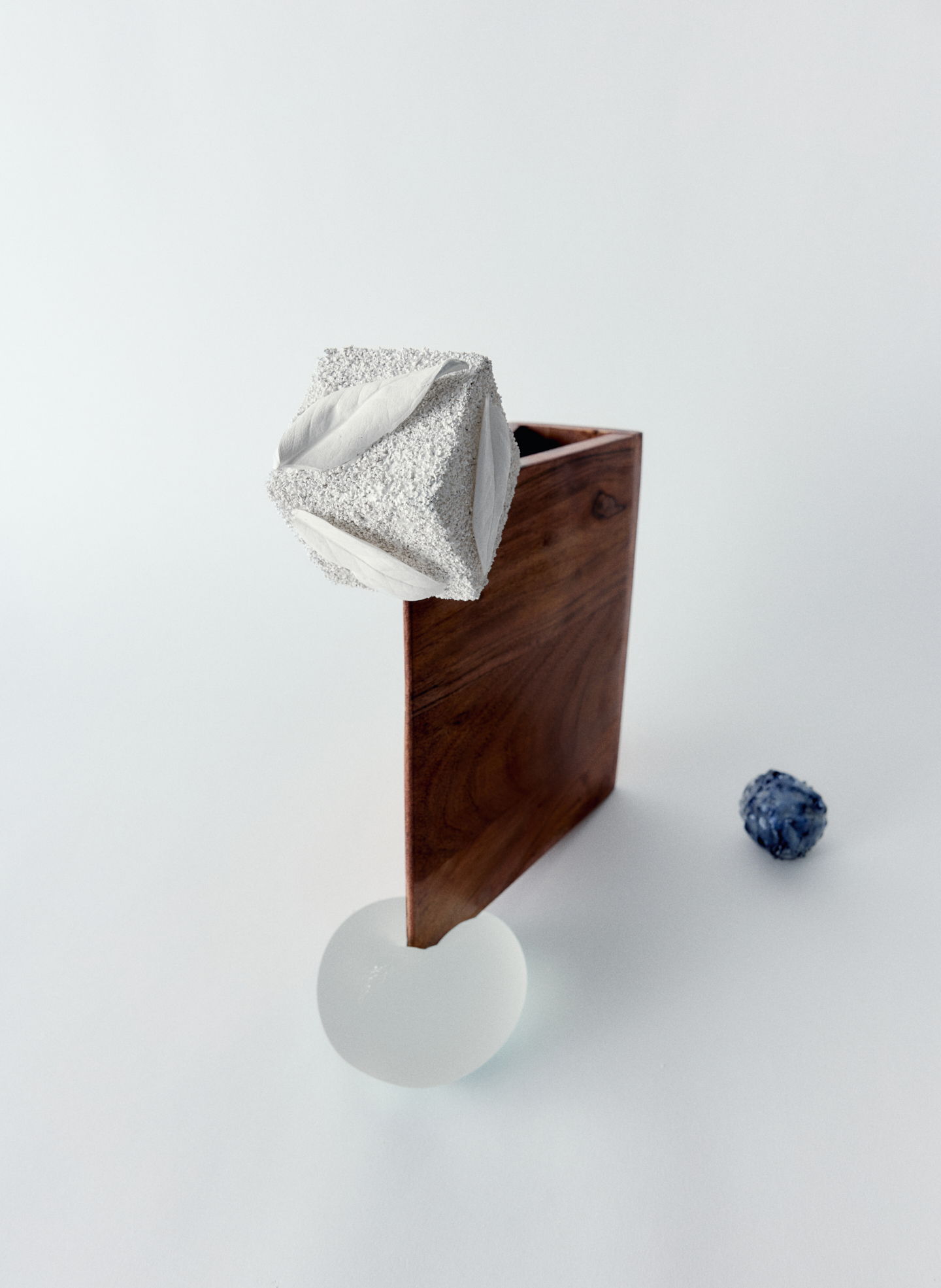 Abstract composition with a wooden box, a silver object, and a round glass piece.