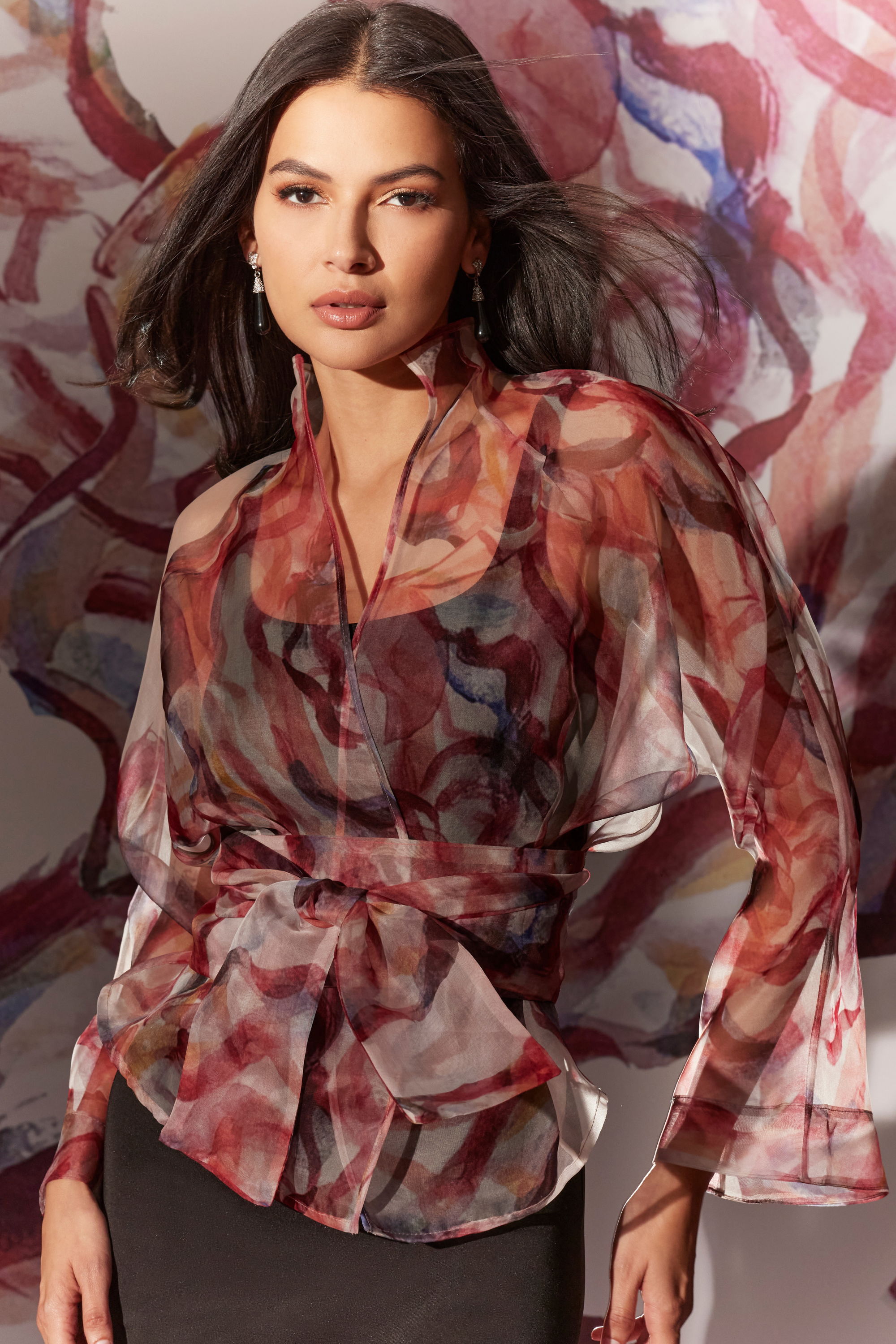 Model wearing a flowing, patterned blouse against a colorful background.