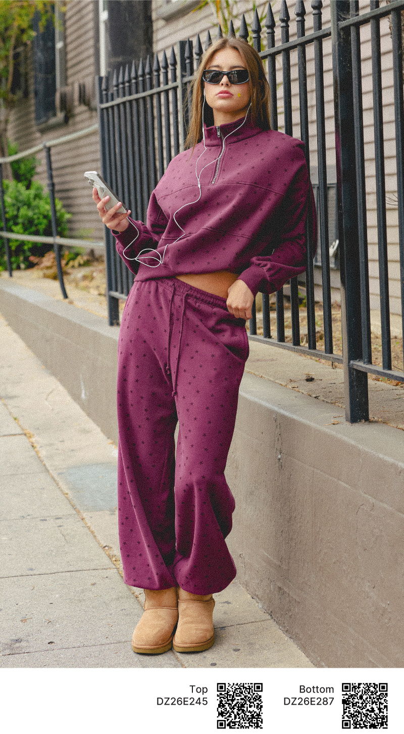 Person in purple outfit and sunglasses, holding a phone, standing on sidewalk.