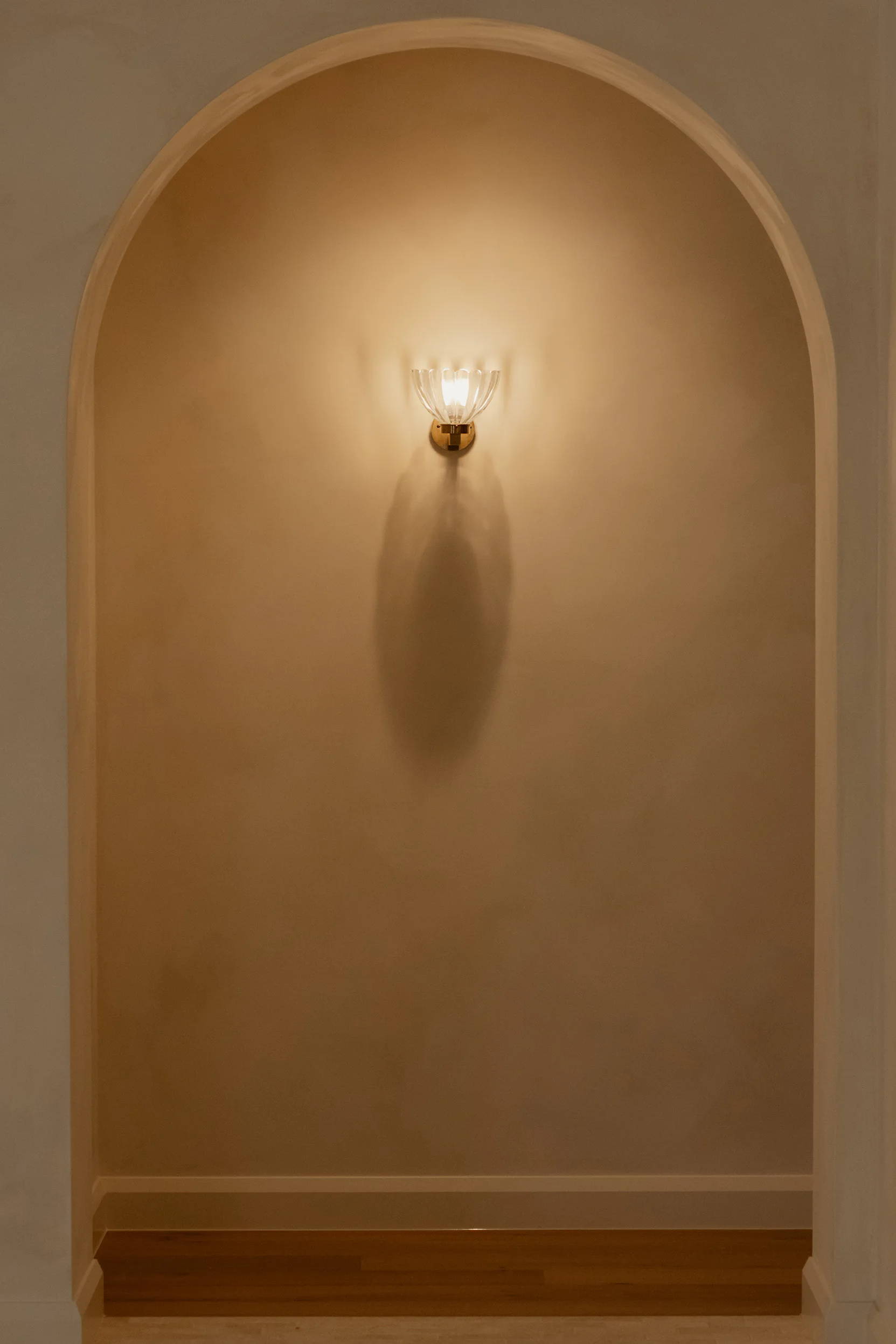 A wall with an arched niche and a single light fixture.