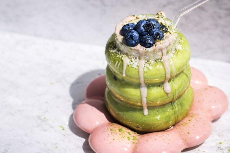 Stack of colorful pastries topped with blueberries on a pink plate.