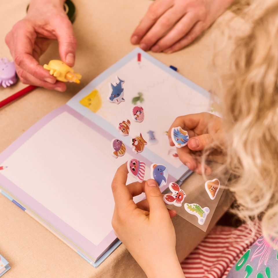 Children placing stickers in a scrapbook with colorful decorations.