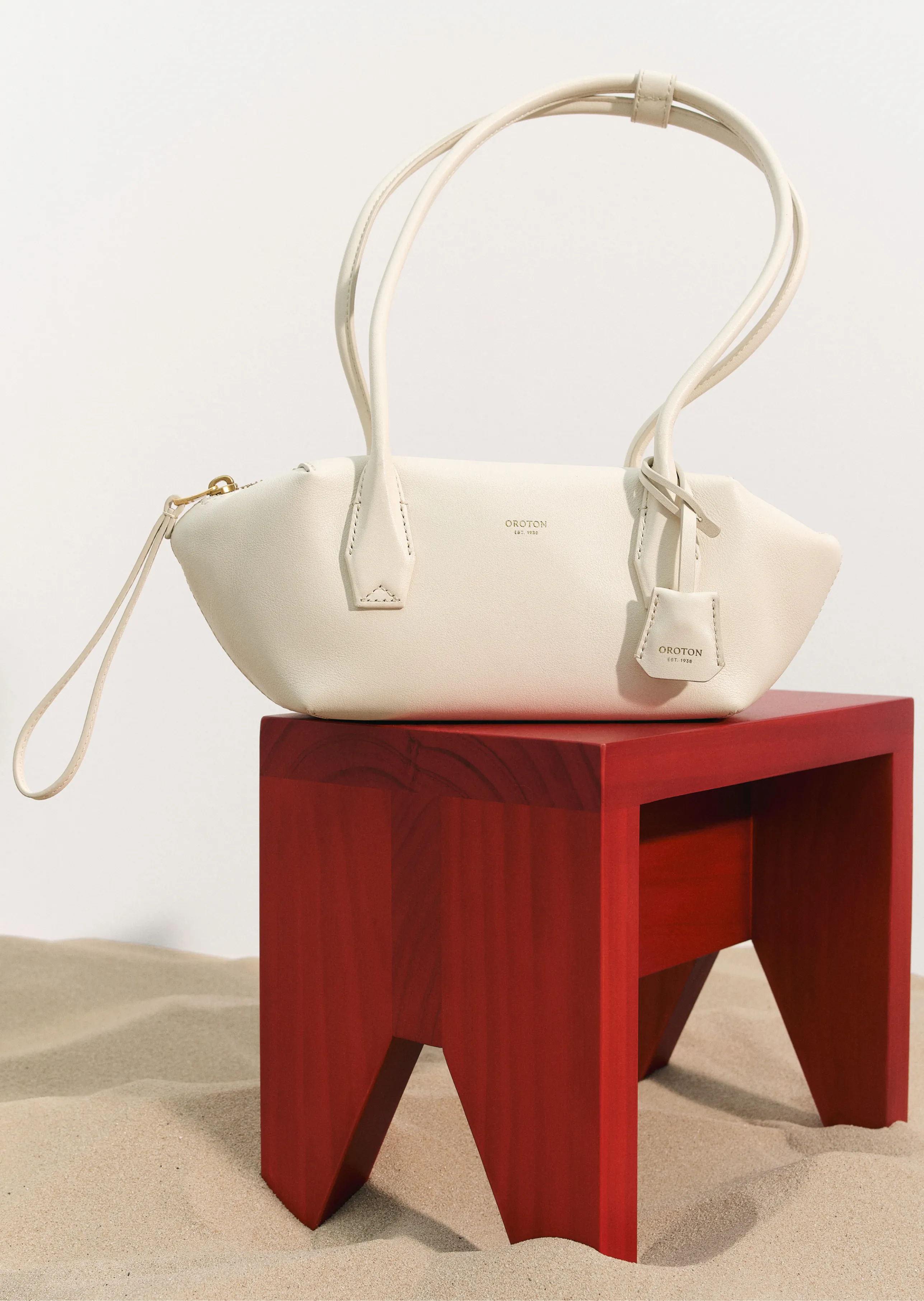A white handbag on a red wooden stool in a sandy setting.