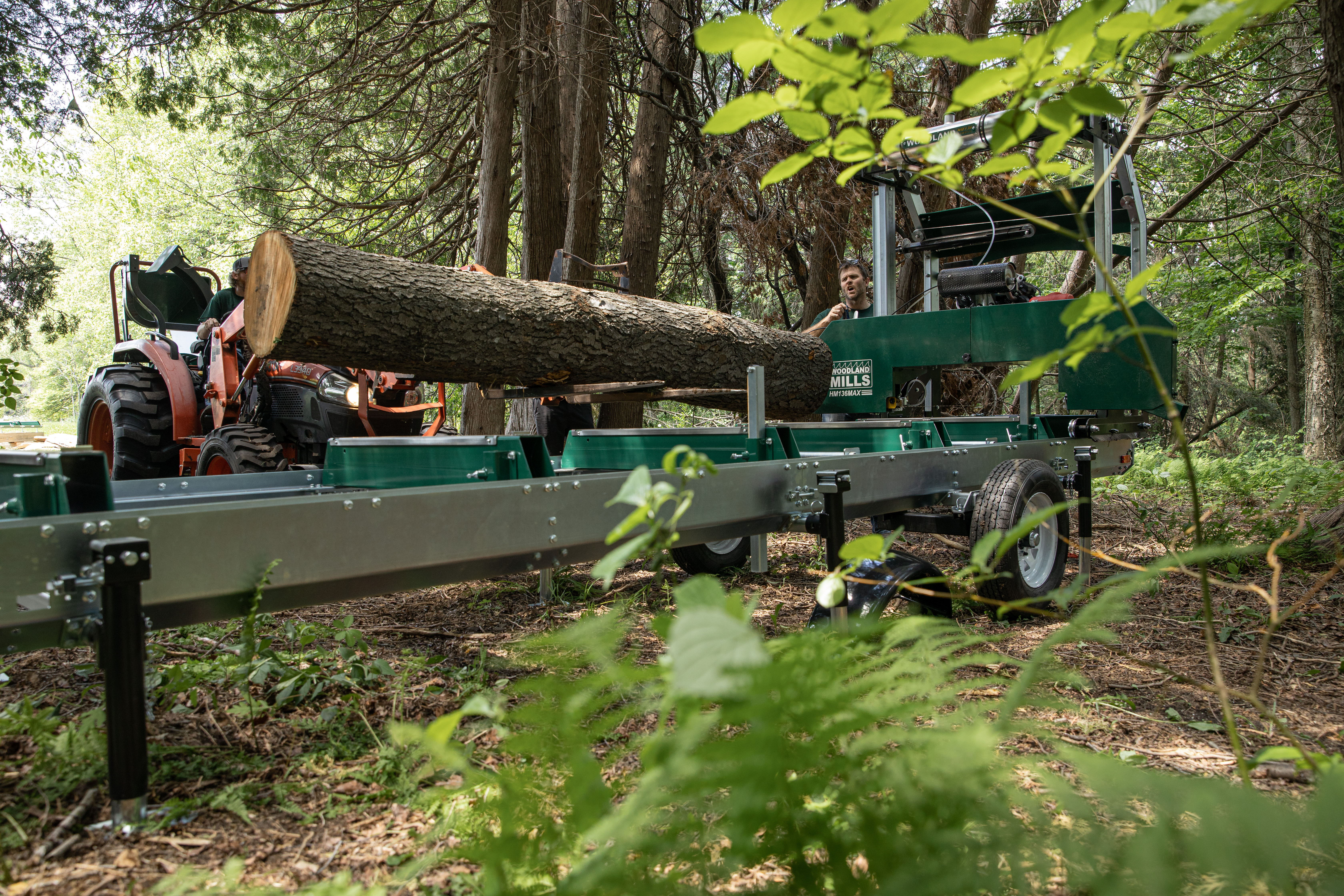 A log is being processed by a Woodland Mills portable sawmill in a forested area.