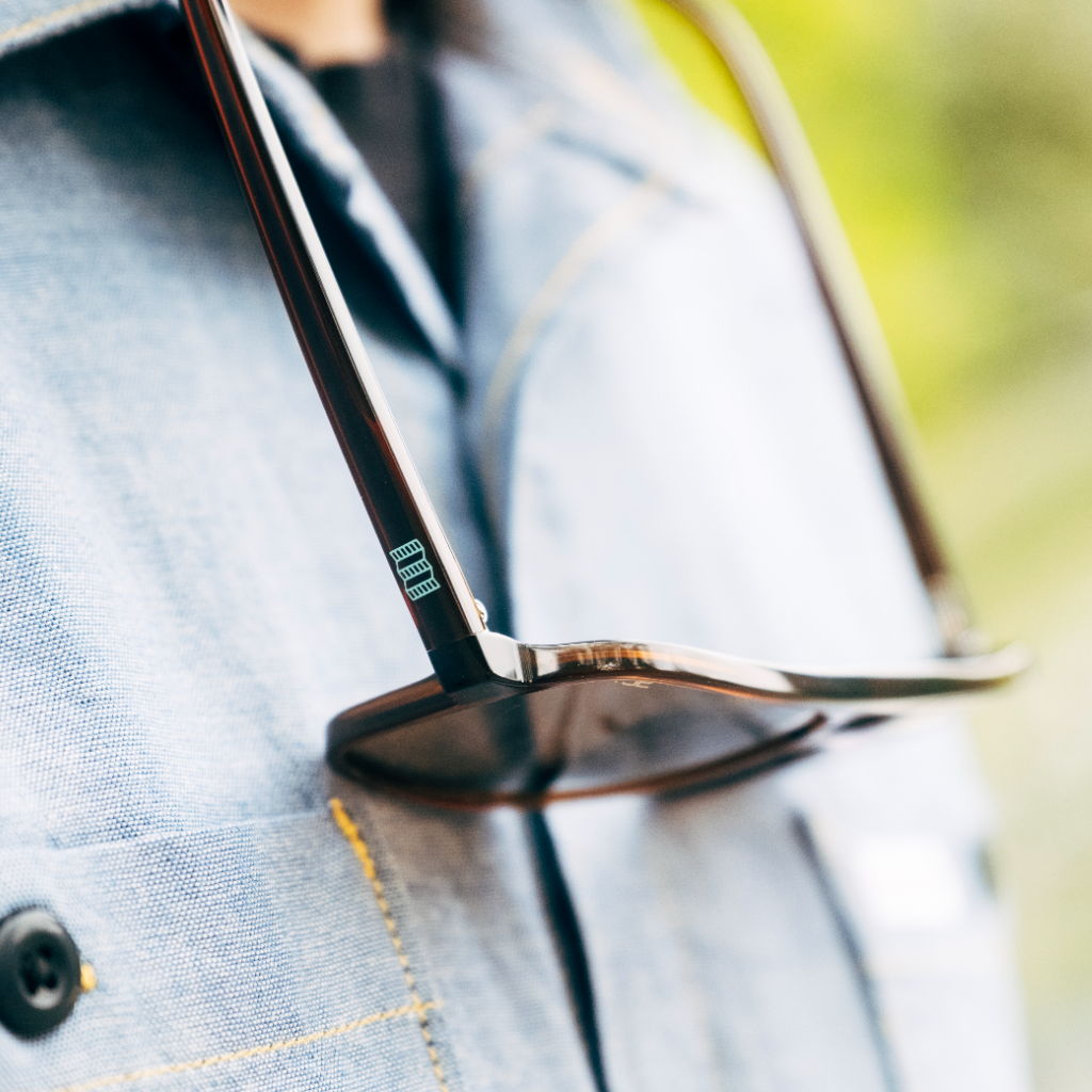 Sunglasses resting on a person's shirt collar outdoors.