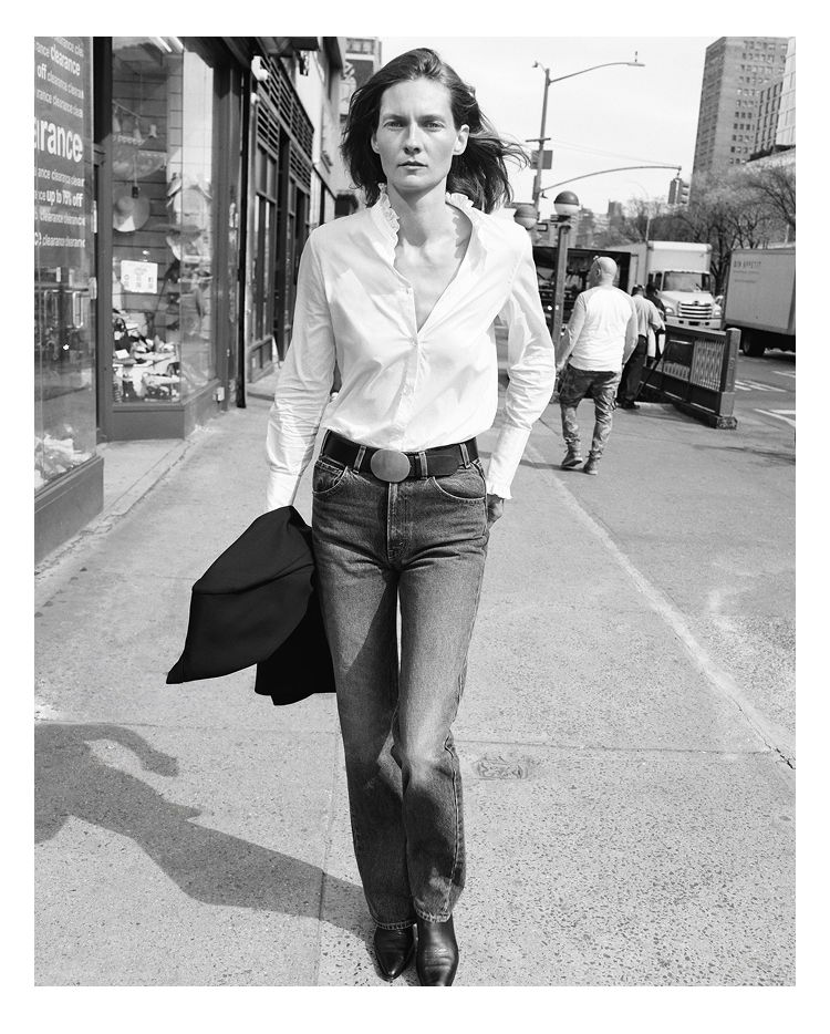 A person walking on the street, wearing a white shirt and jeans.