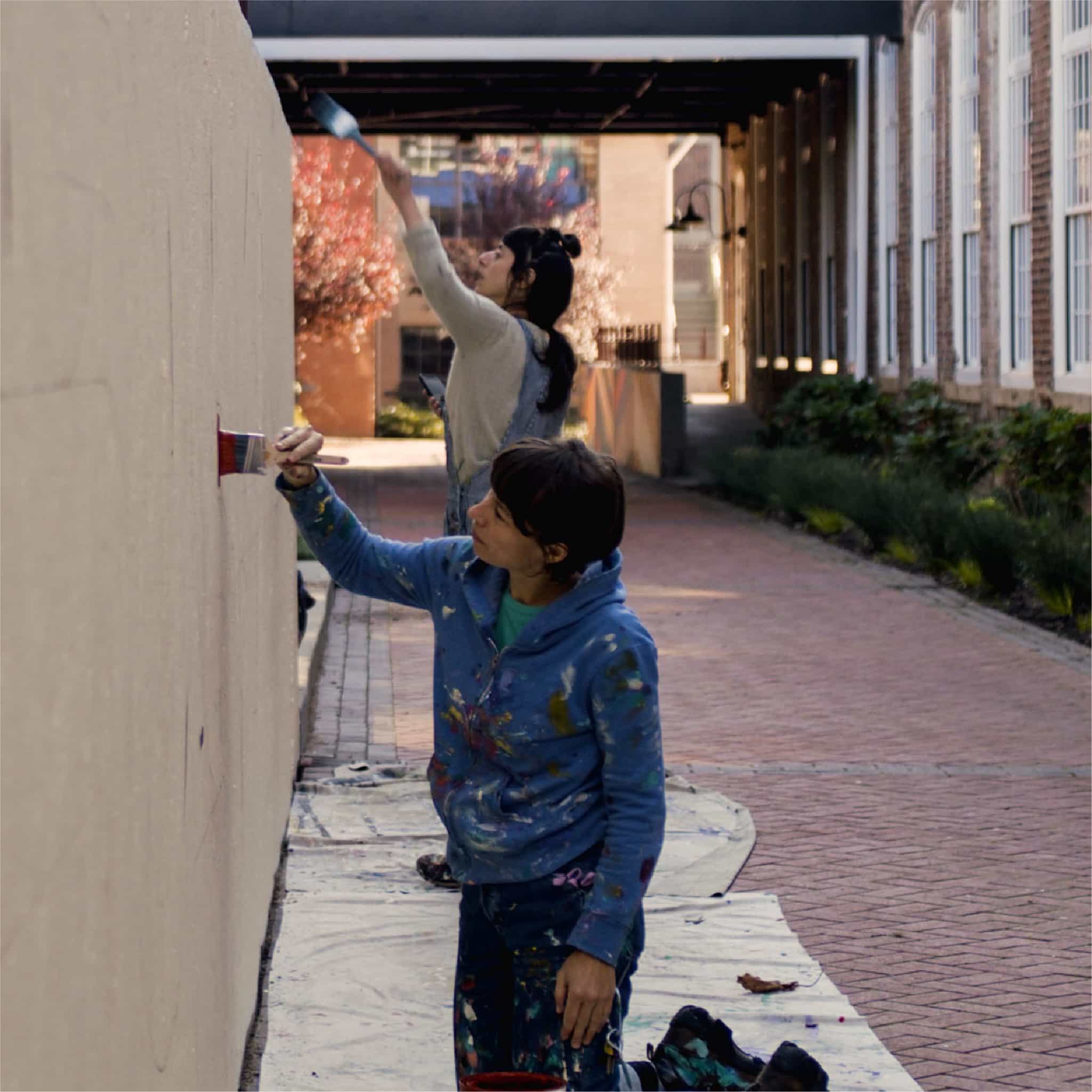 Jessie & Katey painting mural on wall