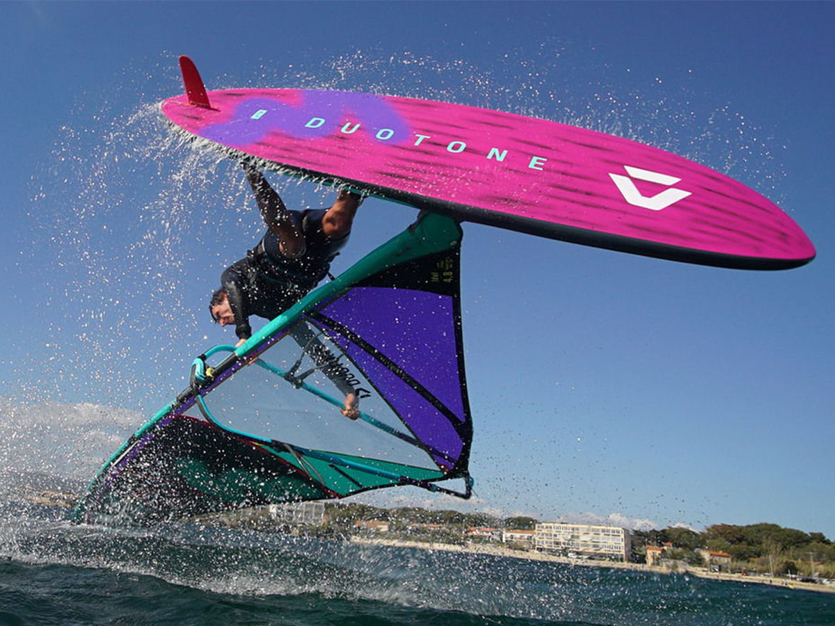 A windsurfer performing a jump over water with a colorful sailboard.