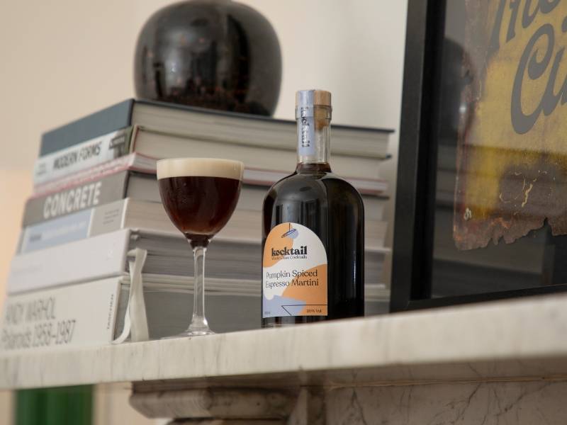 Pumpkin Spiced Espresso Martini bottle on a shelf with drink next to it in front of books