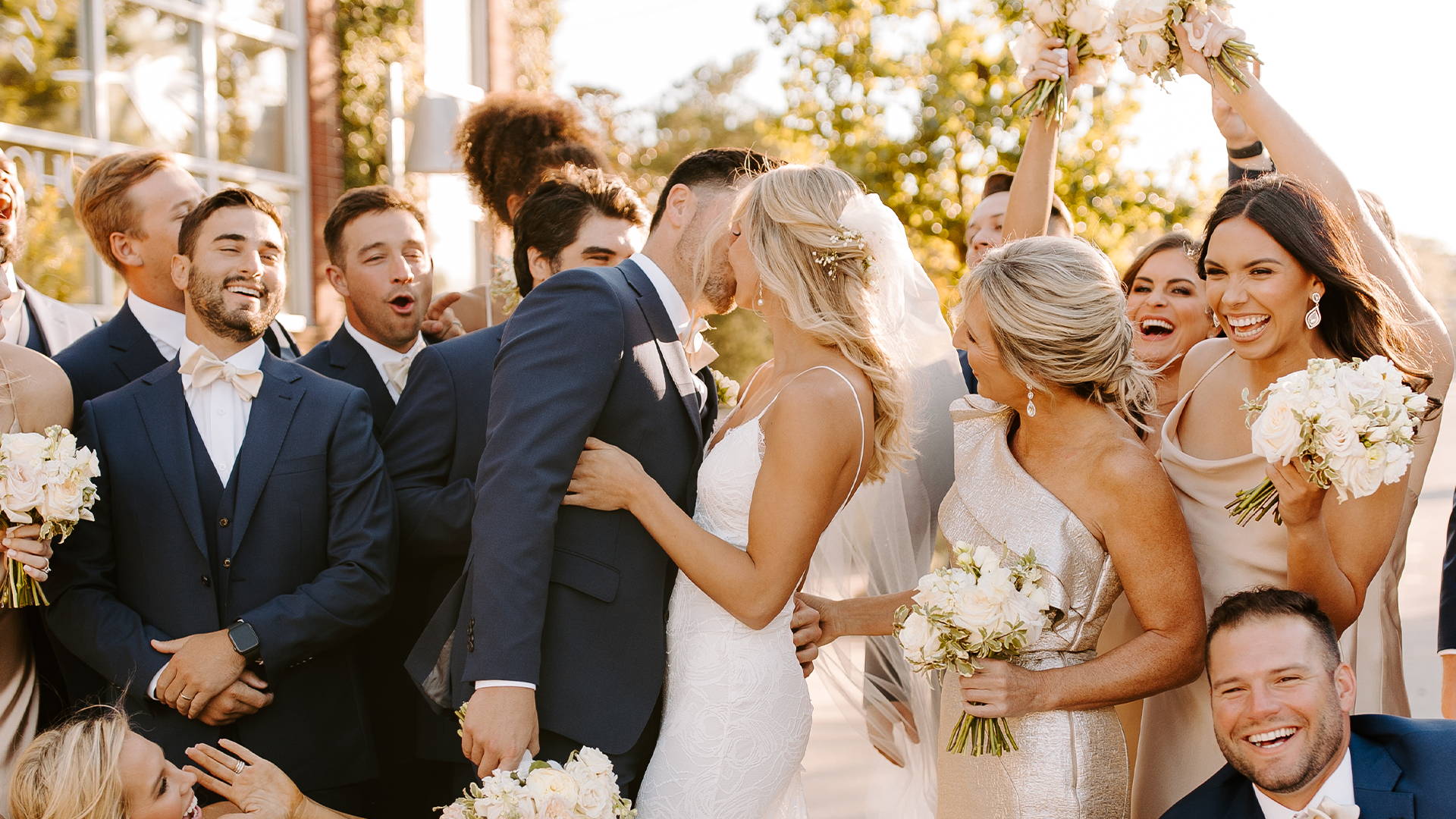 Groom and bride kiss as the wedding party cheer on