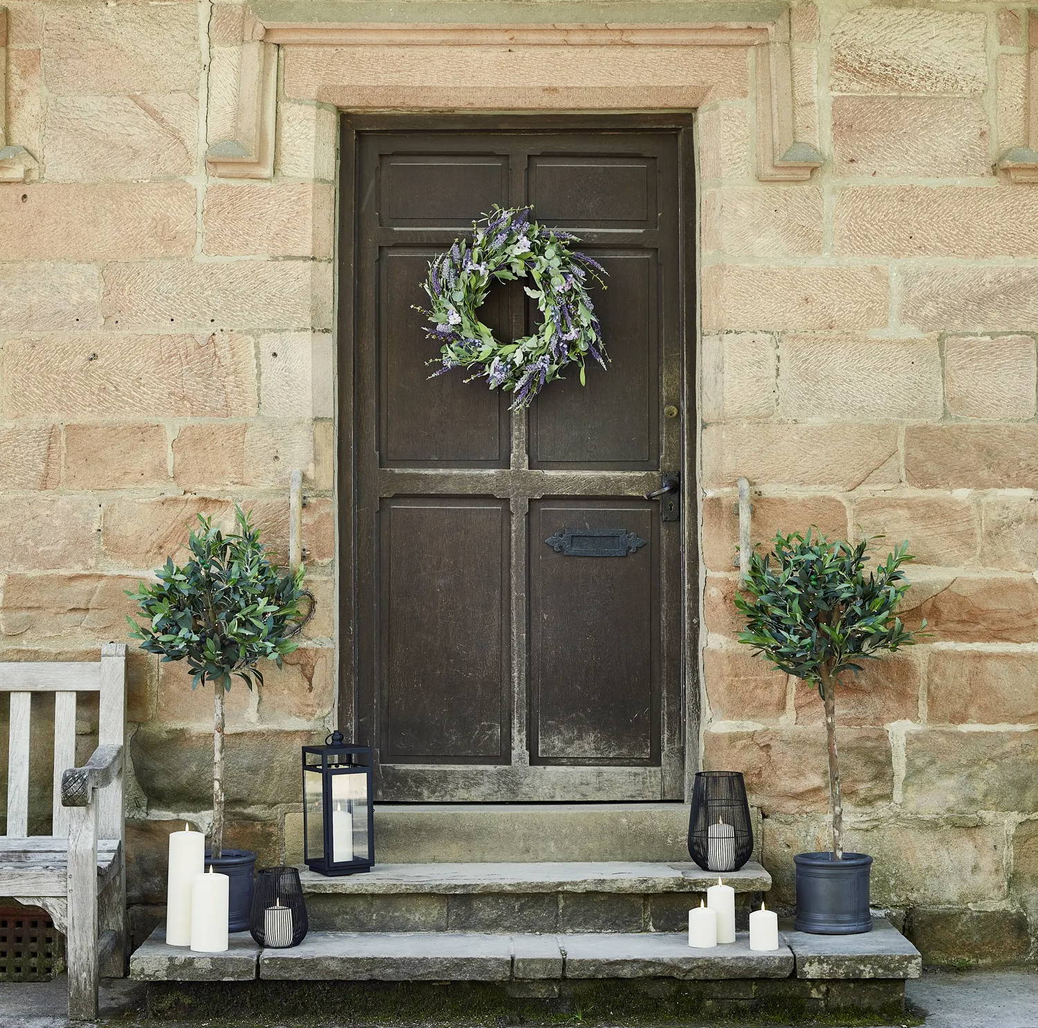 Summer doorway with a lavender wreath and lanterns with 2 shrubs besides the door.
