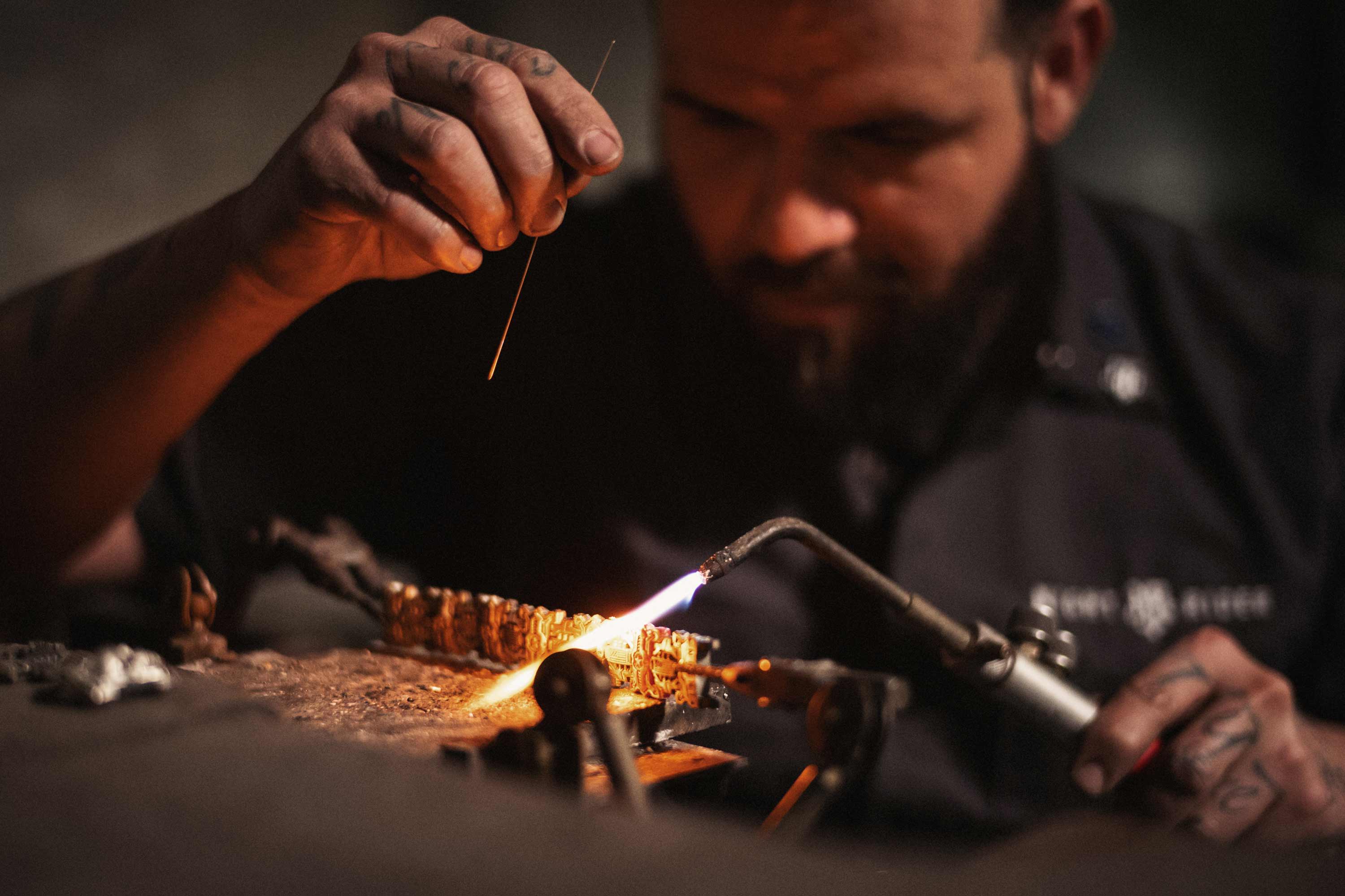 A bench jeweler uses a torch to weld a bracelet