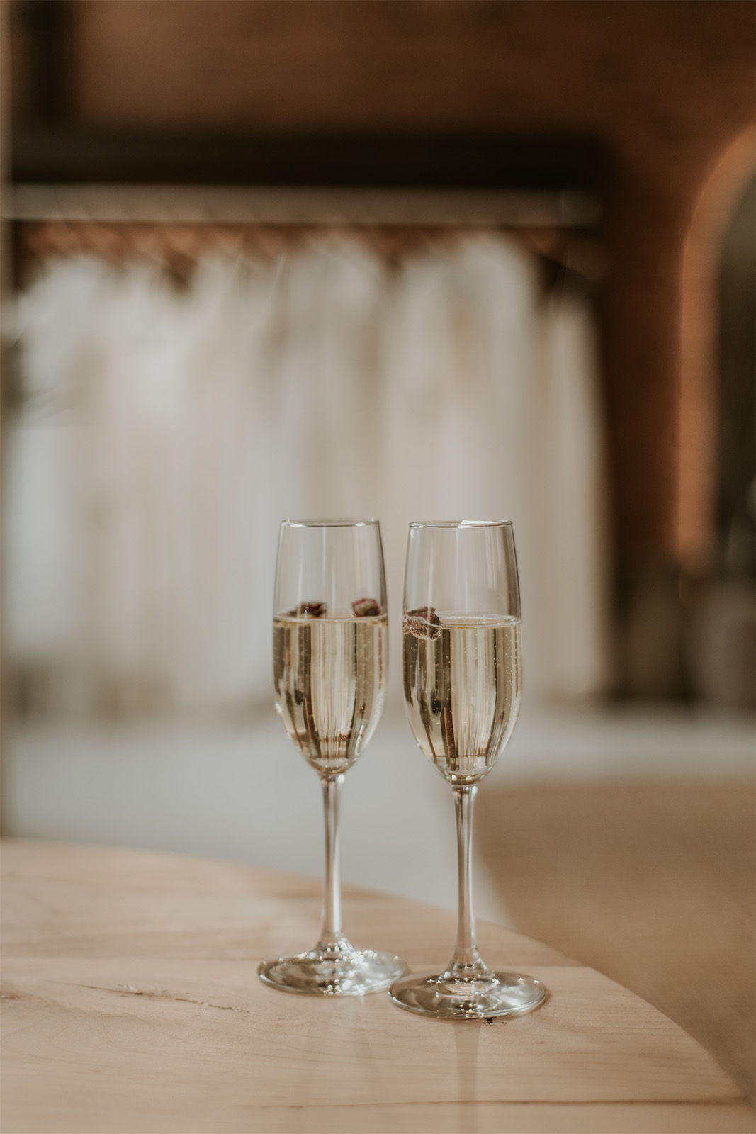 Two champagne glasses on a table with wedding dresses in the background.