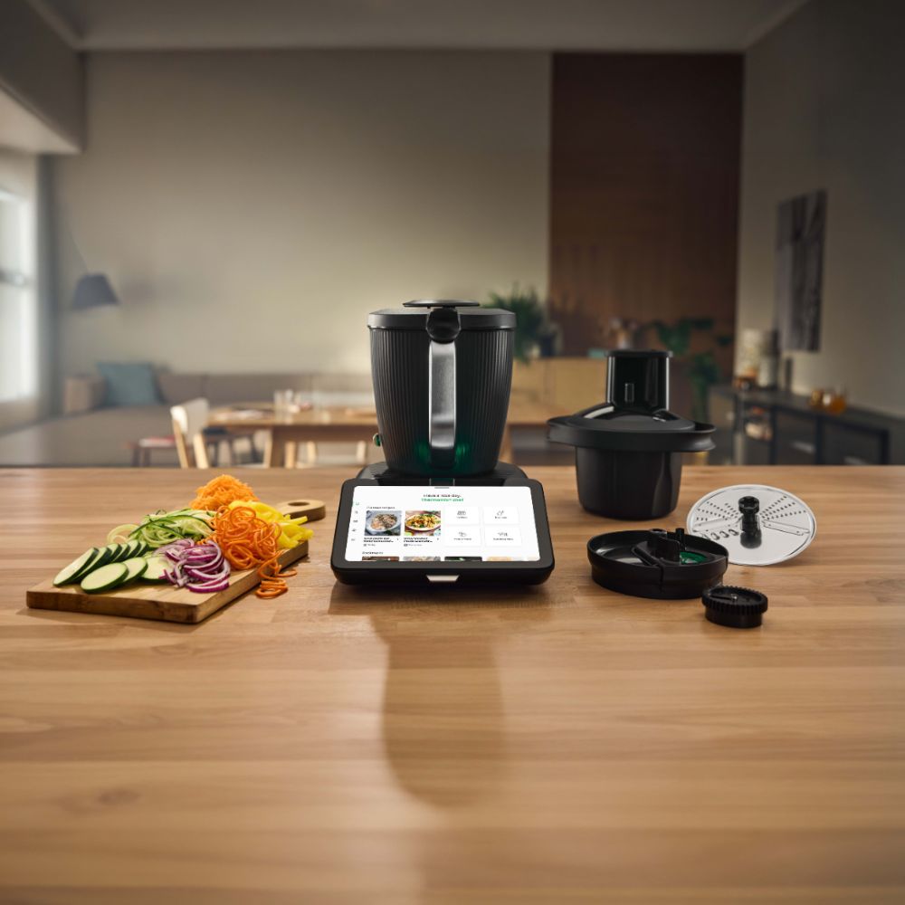 A kitchen countertop with a cooking device and various vegetables arranged.