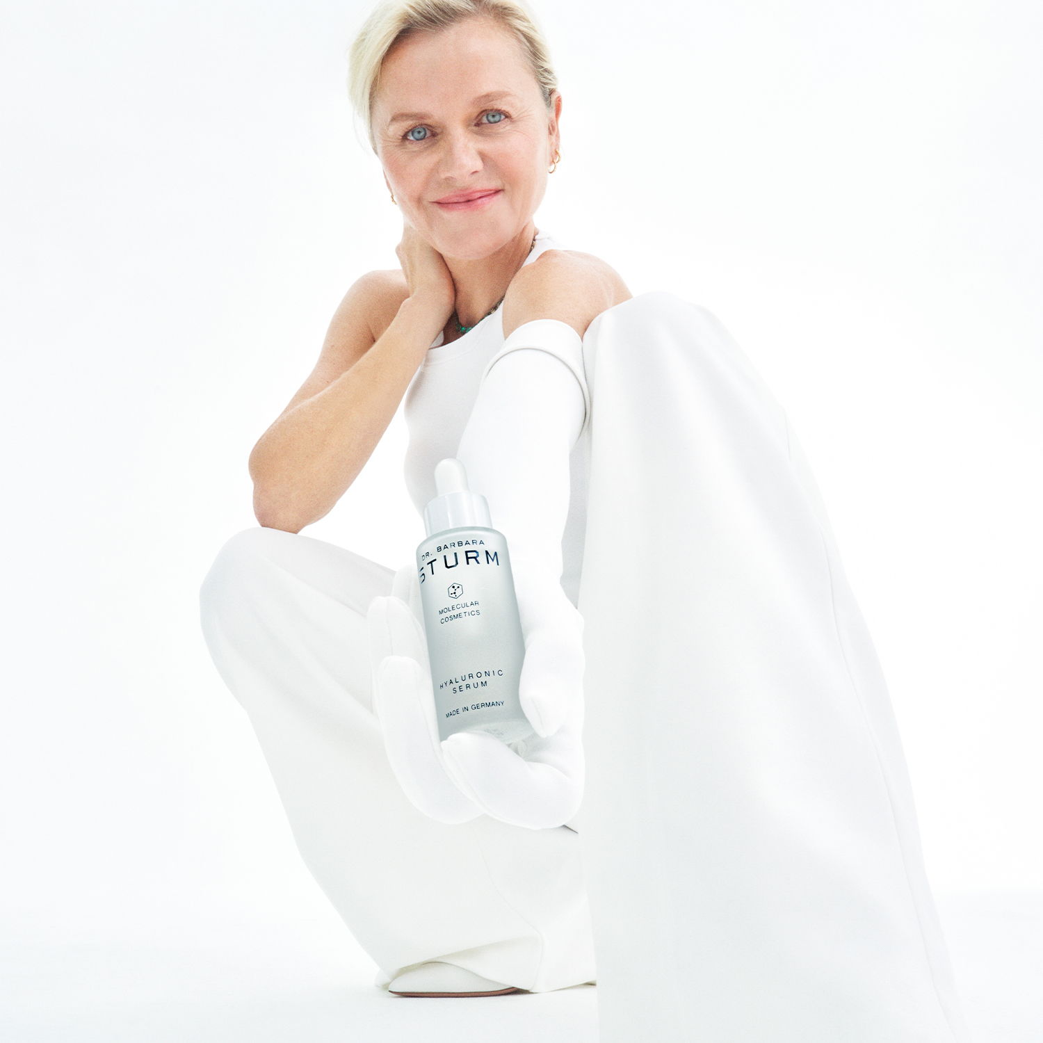 Woman in white outfit posing with a bottle against a white background.