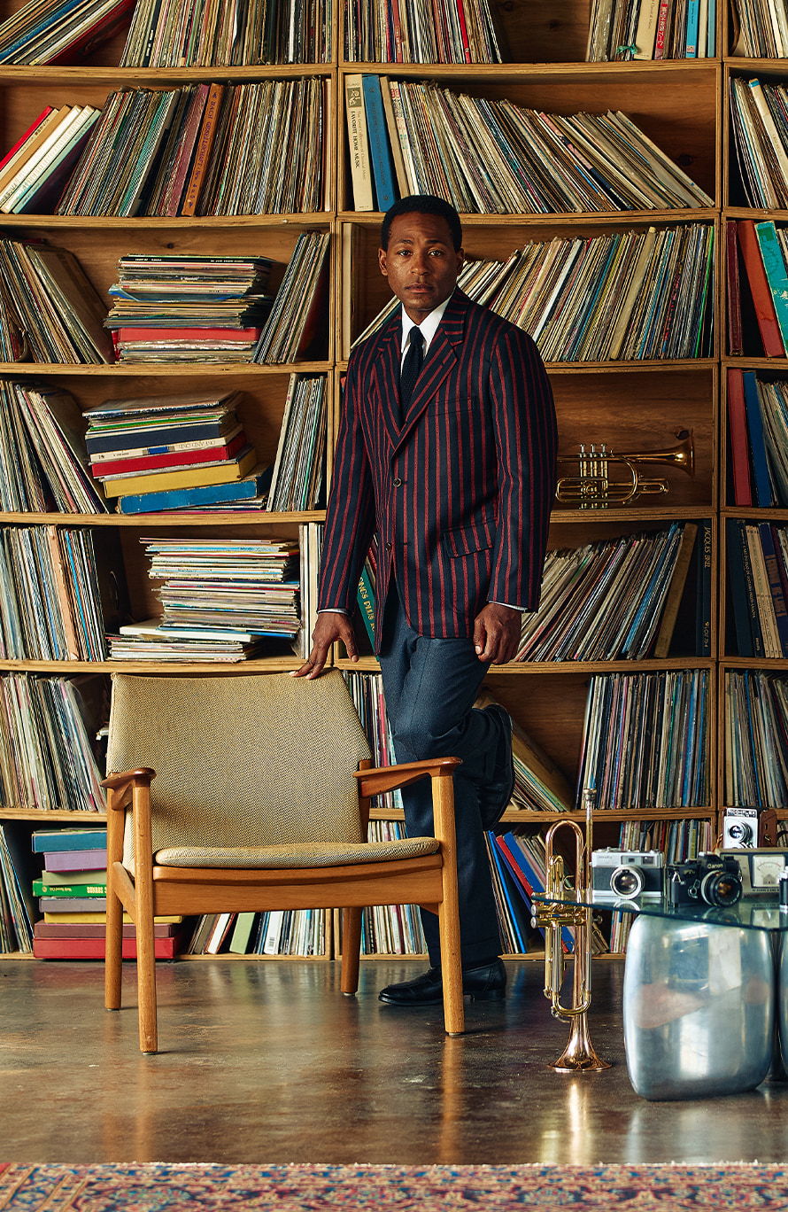 Man in a striped suit standing near a shelf of vinyl records.