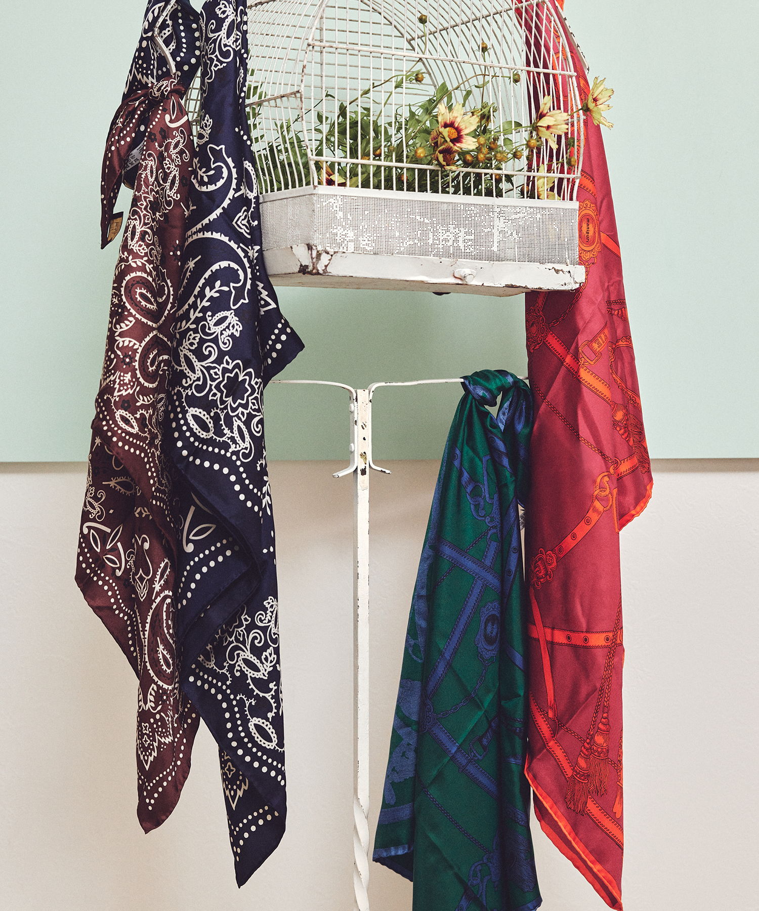 PIMENTÉ 3周年限定コレクション 2026　Colorful scarves hanging next to a decorative birdcage with plants inside.