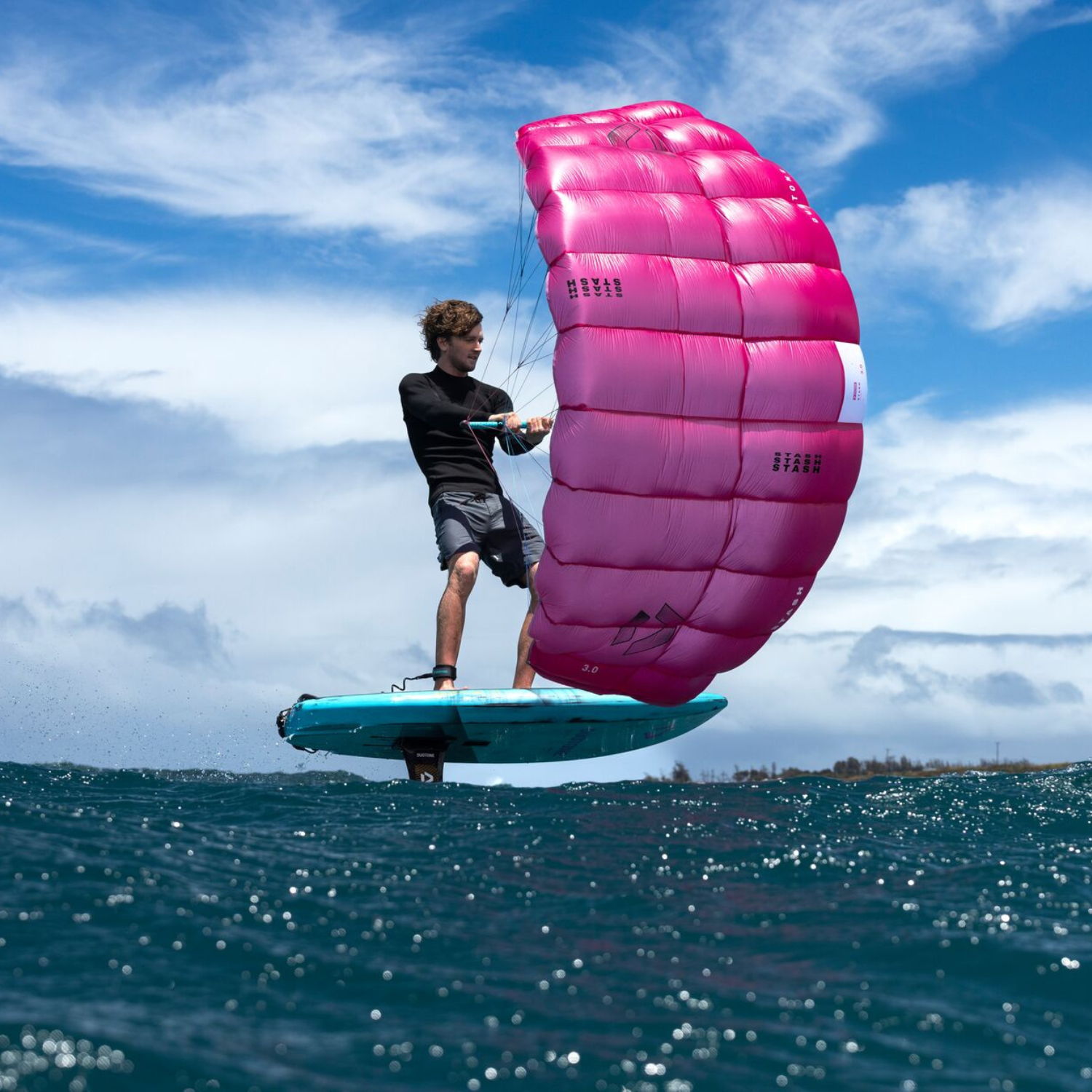 Person parawing on a blue board with a pink wing over the ocean.