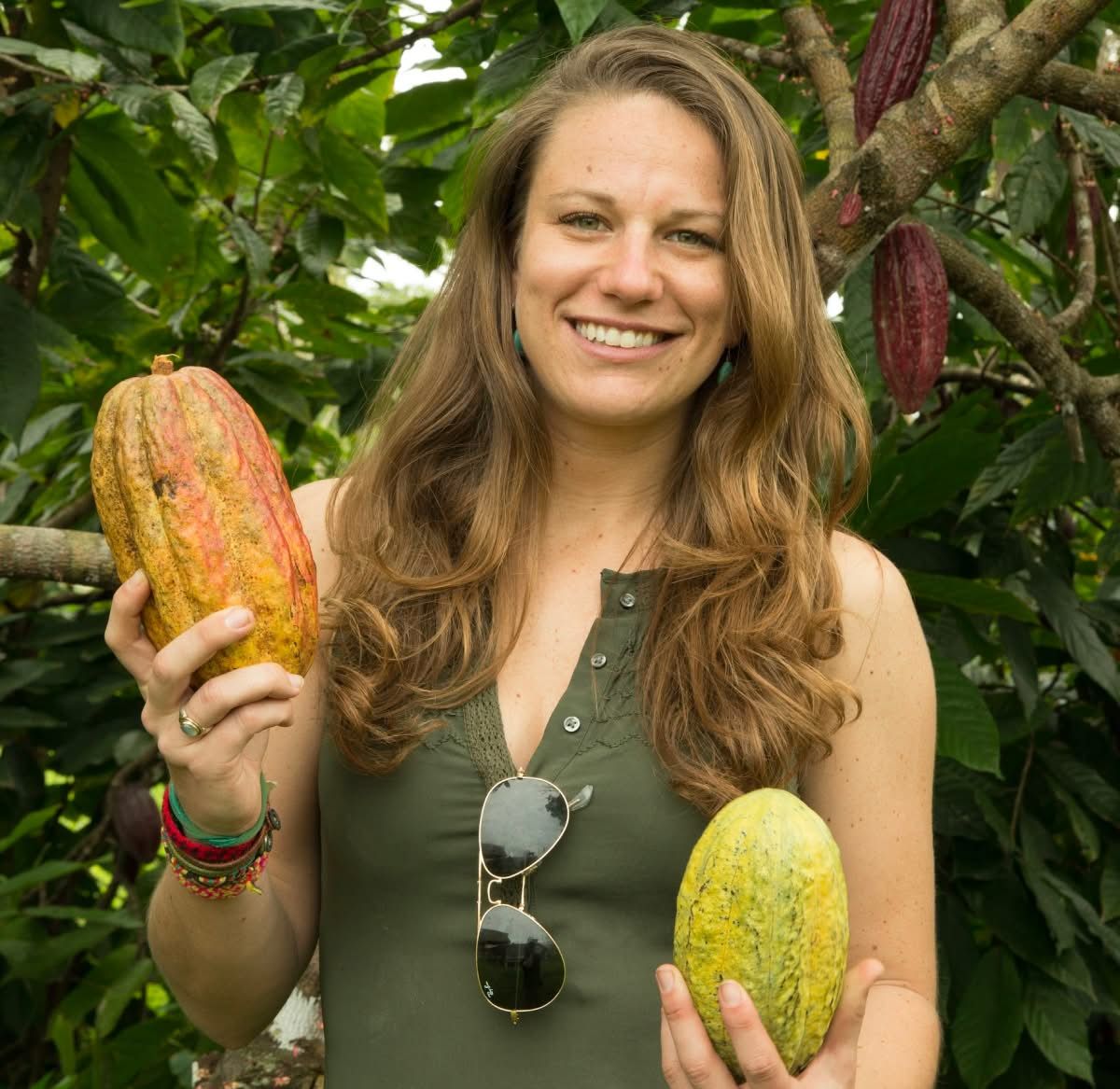 Woman holding cocoa pods in a lush green environment.