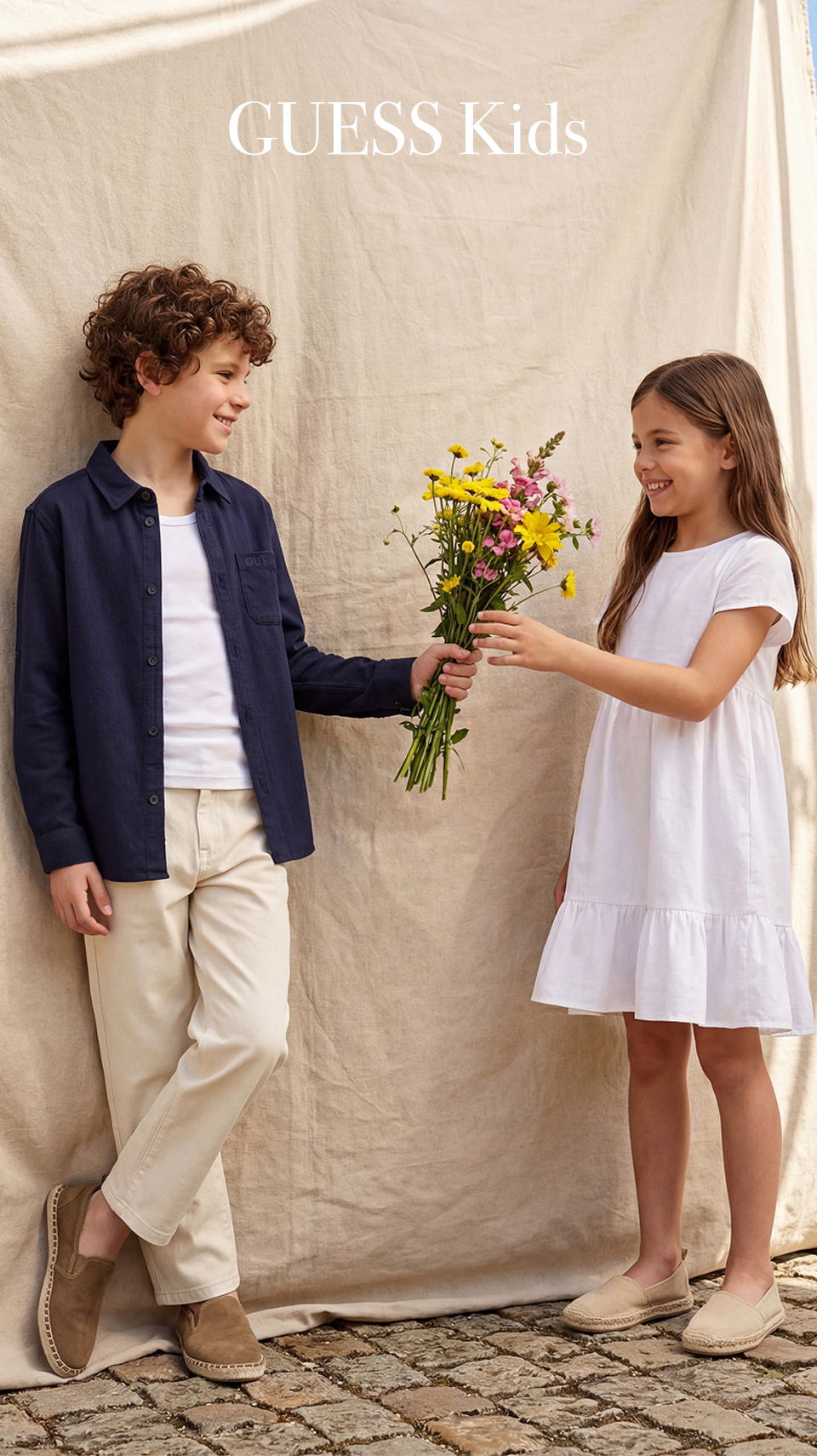 Two children exchanging flowers in casual clothing against a neutral backdrop.