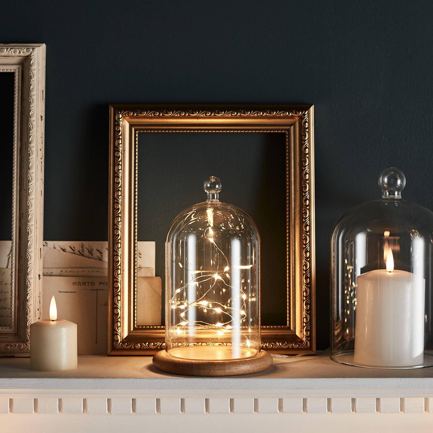 A dome filled with fairy lights on a mantlepiece with candles and photo frames.