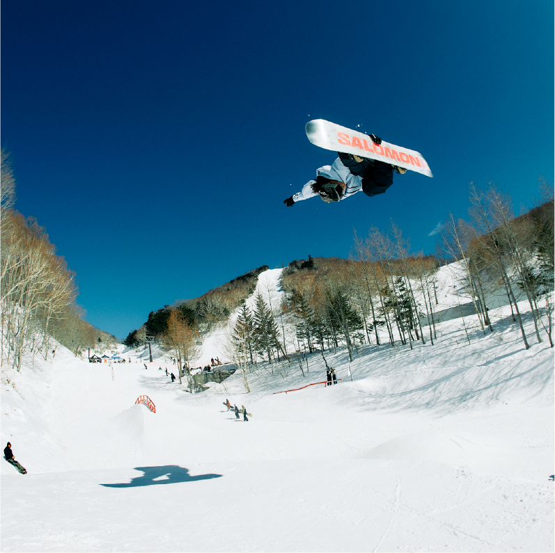 Snowboarder performing a trick in mid-air over a snowy slope.