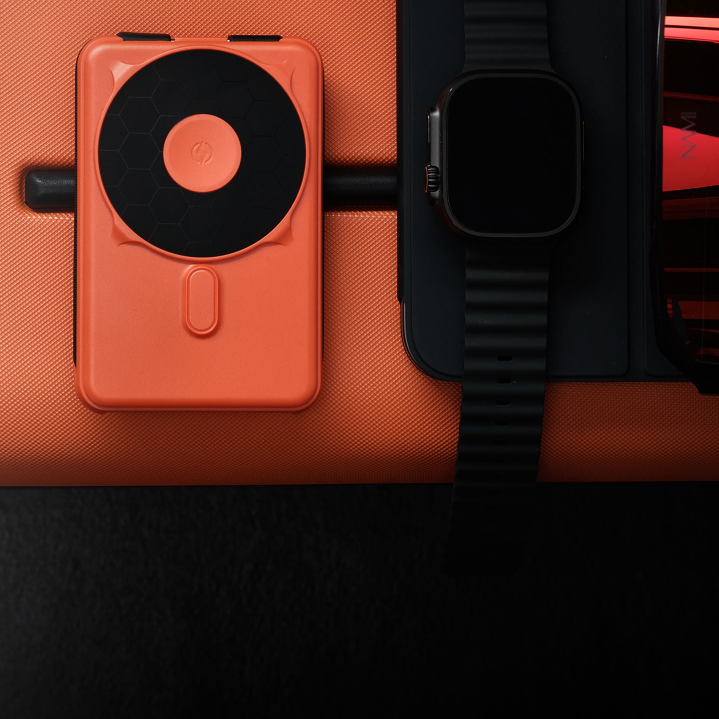 An orange device next to a watch on a black surface.