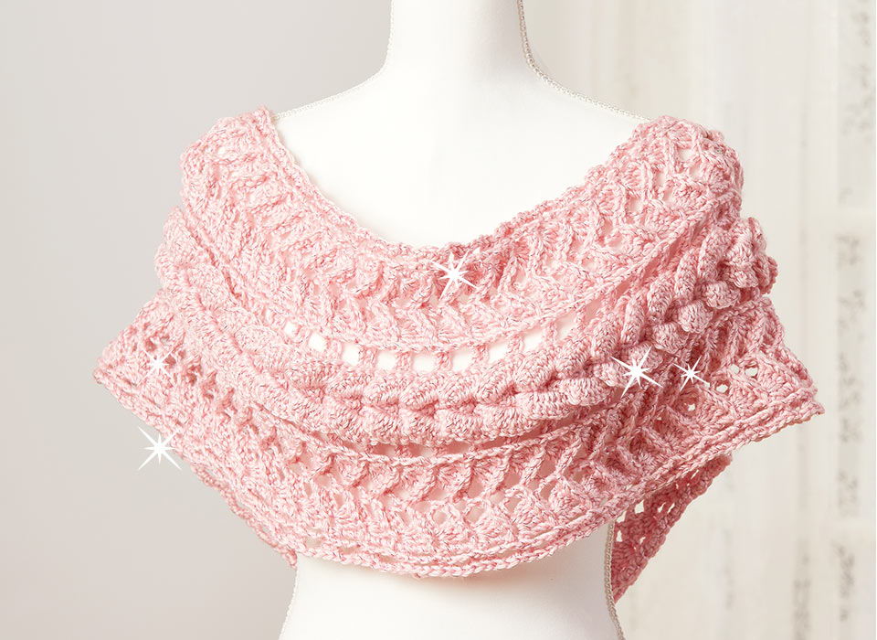 Pink knitted shawl draped over a mannequin against a light background.
