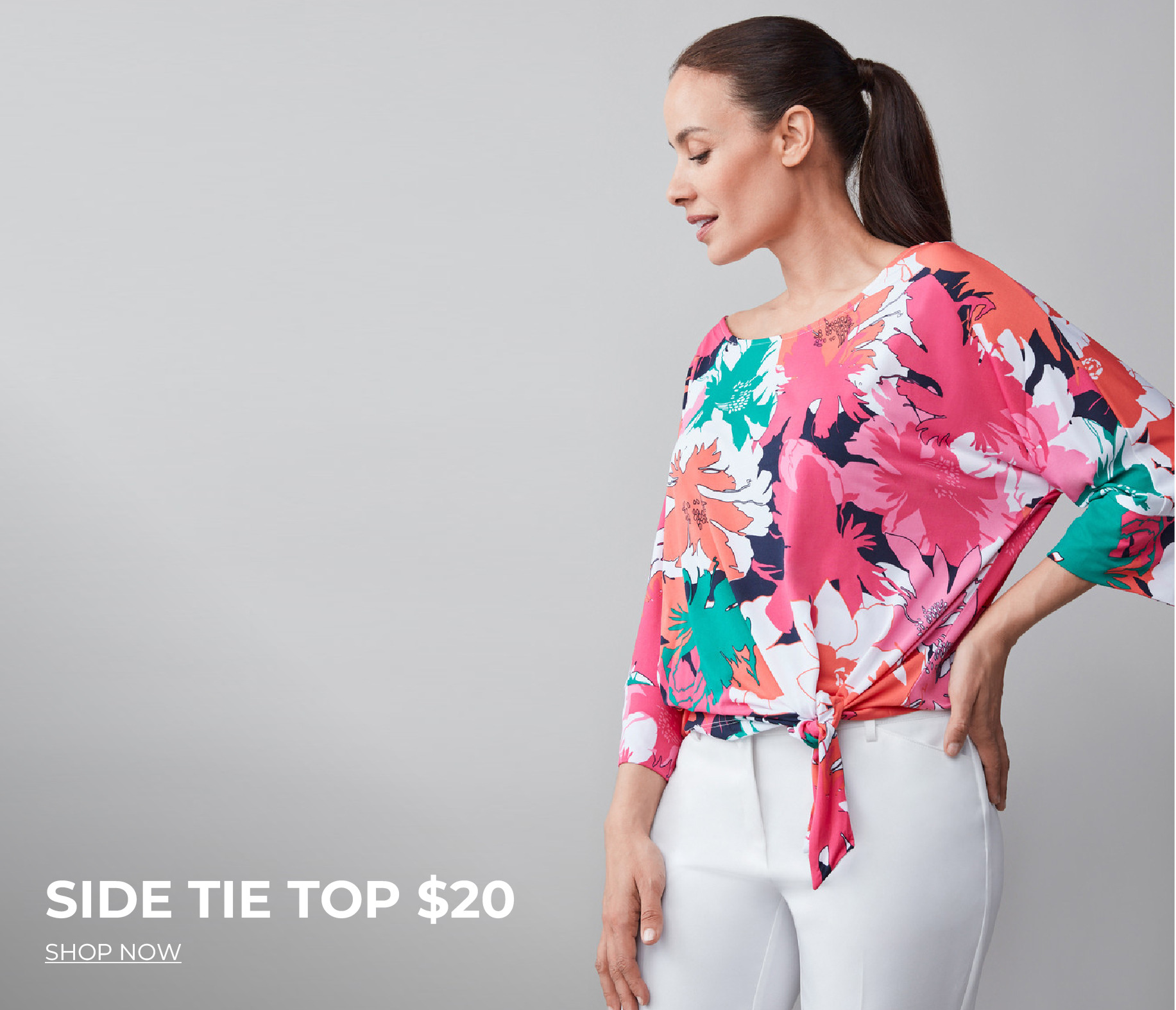 Model wearing a colorful side tie top with white pants against a gray background.