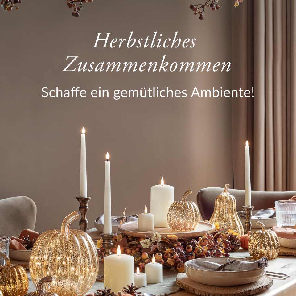Ein herbstlich dekorierter Esstisch mit vertreuten LED Kerzen, Glas- und Filzkürbissen und Herbstkranz 