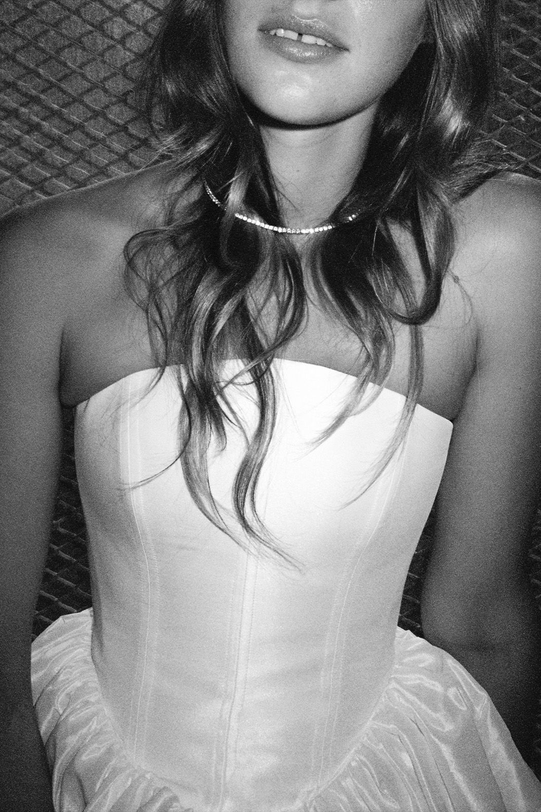 Woman in a strapless white dress with wavy hair, photographed in black and white.