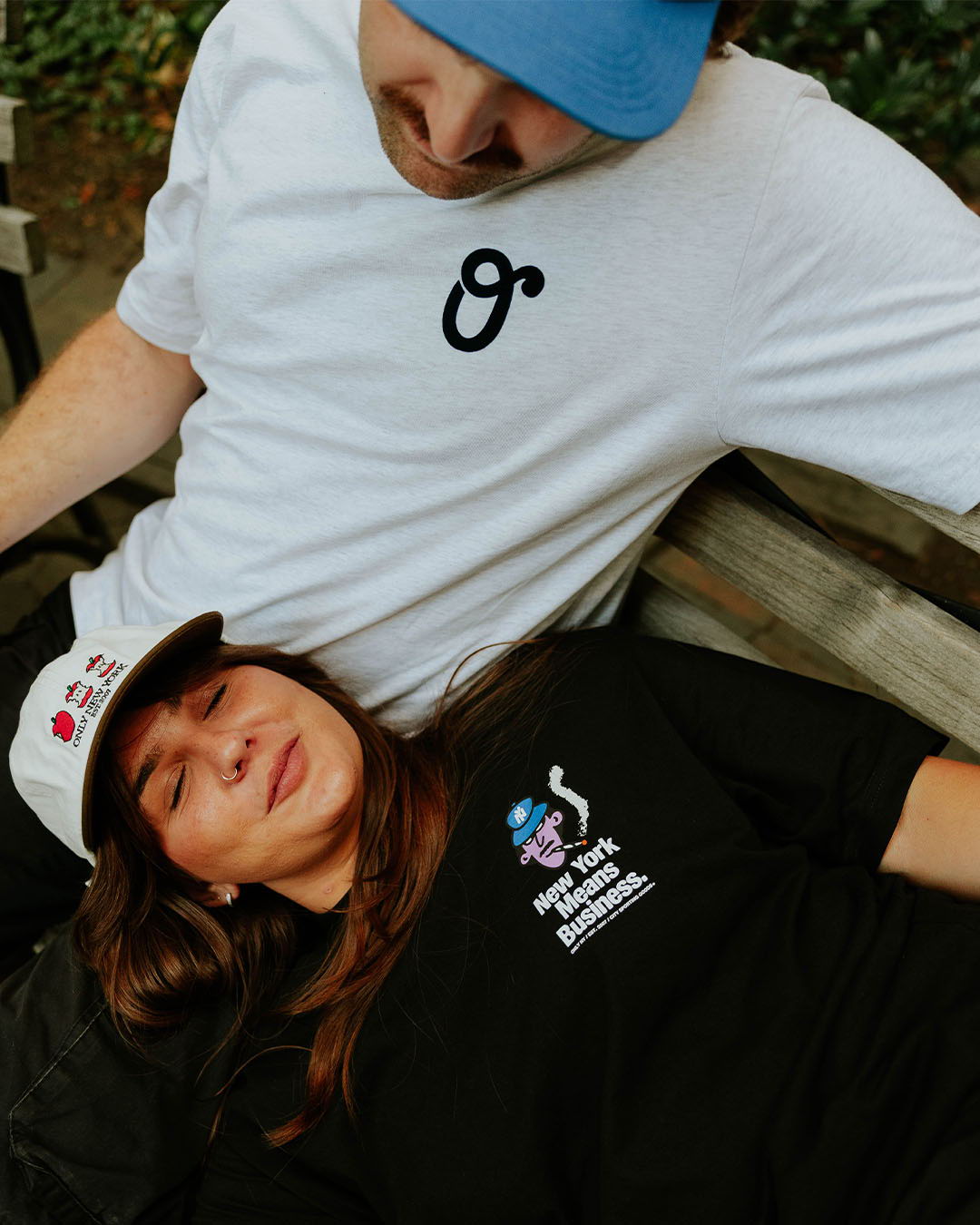 Two people relaxing on a bench, wearing casual clothing and hats.