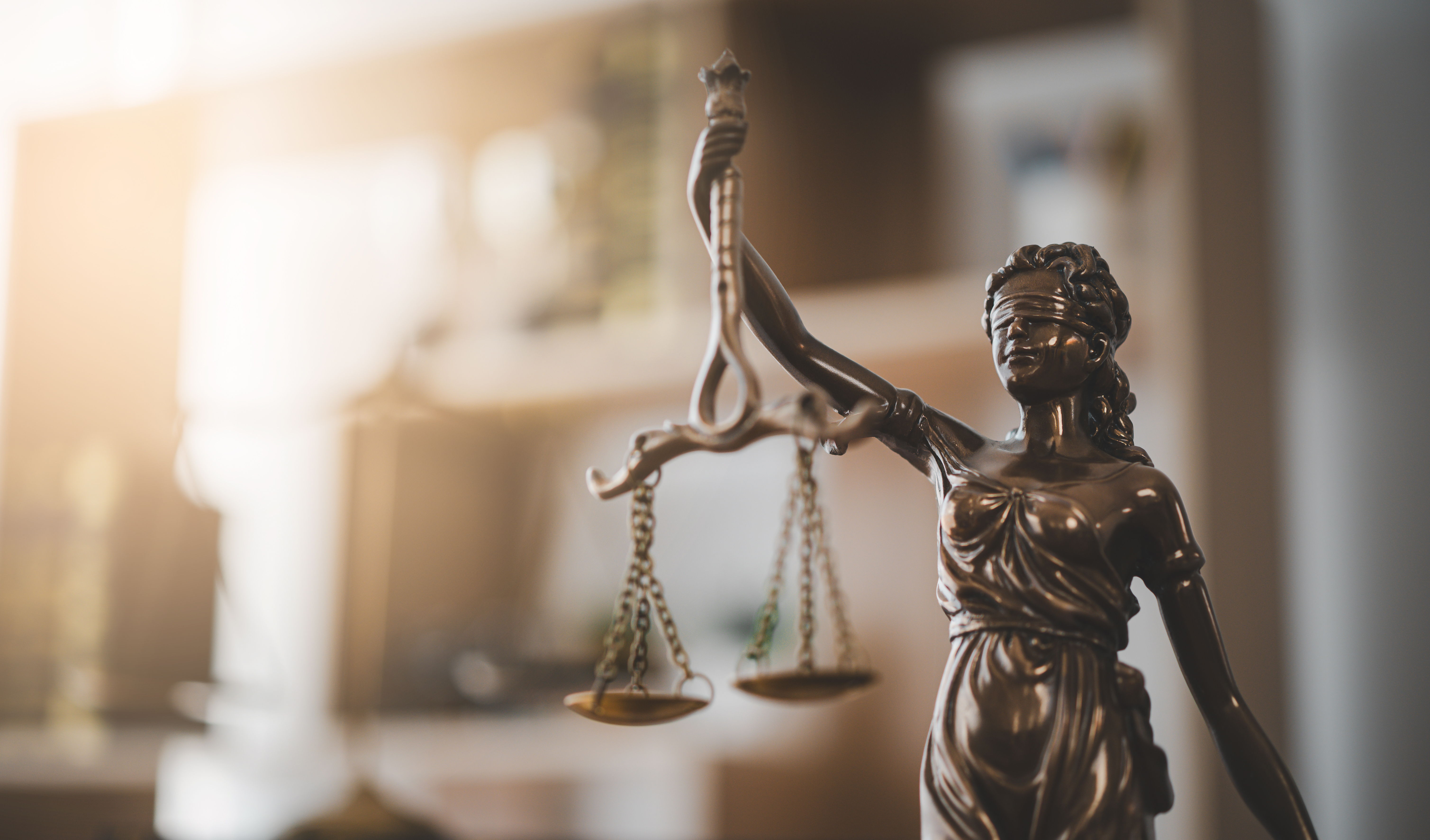 Statue of Lady Justice holding scales in a softly lit environment.