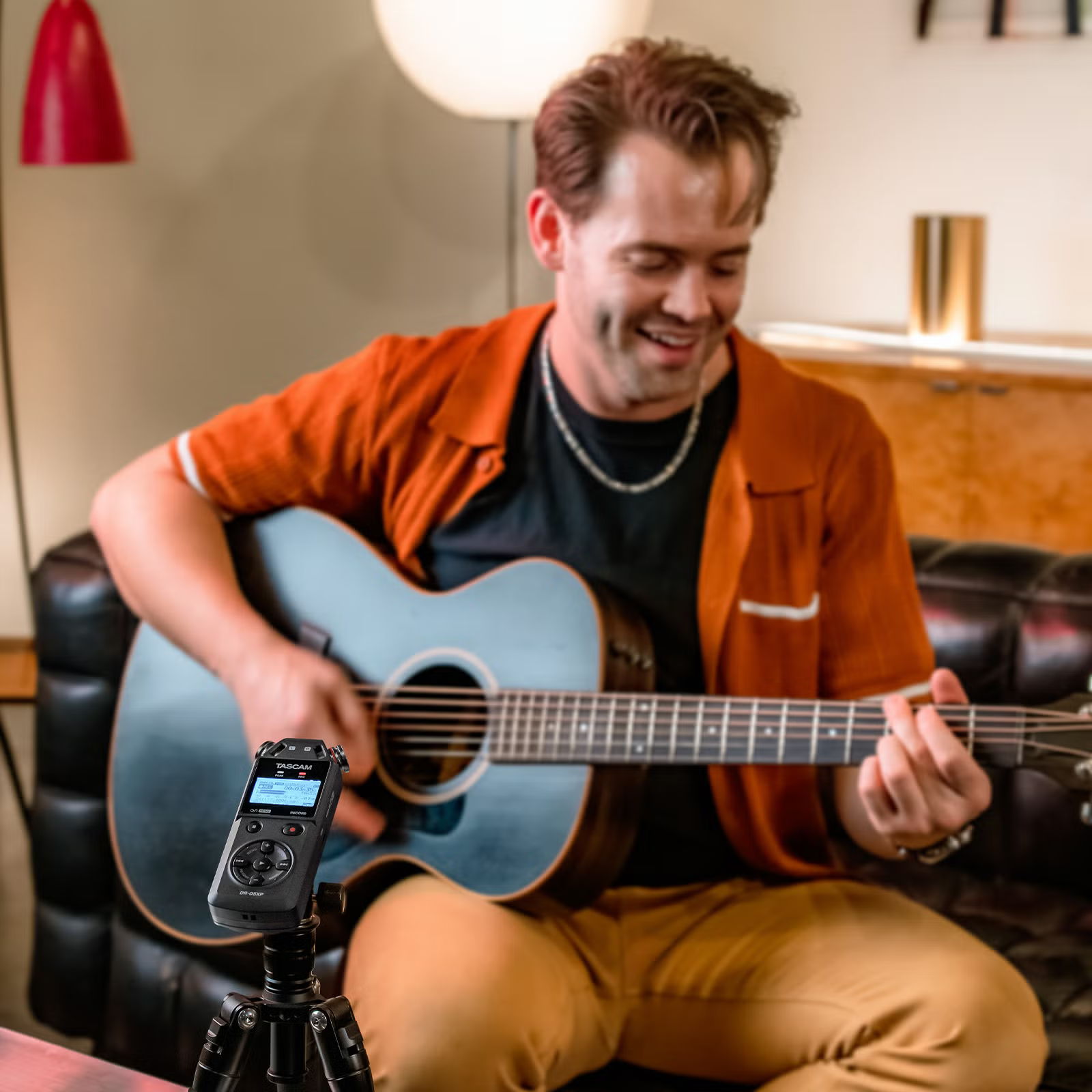 Person playing acoustic guitar while smiling in a cozy setting.