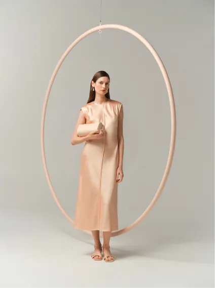 Model in a beige dress standing inside a large circular frame.