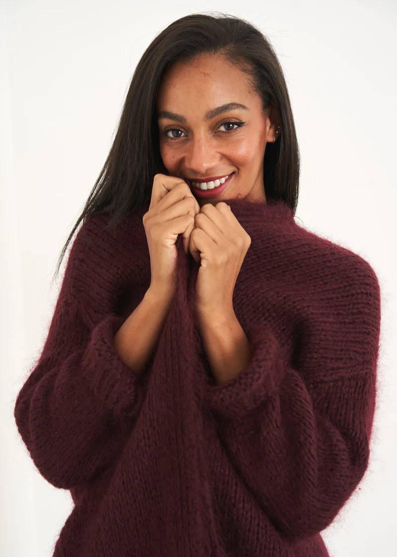A model wearing a chunky,knit overszied cardigan in a plum colour