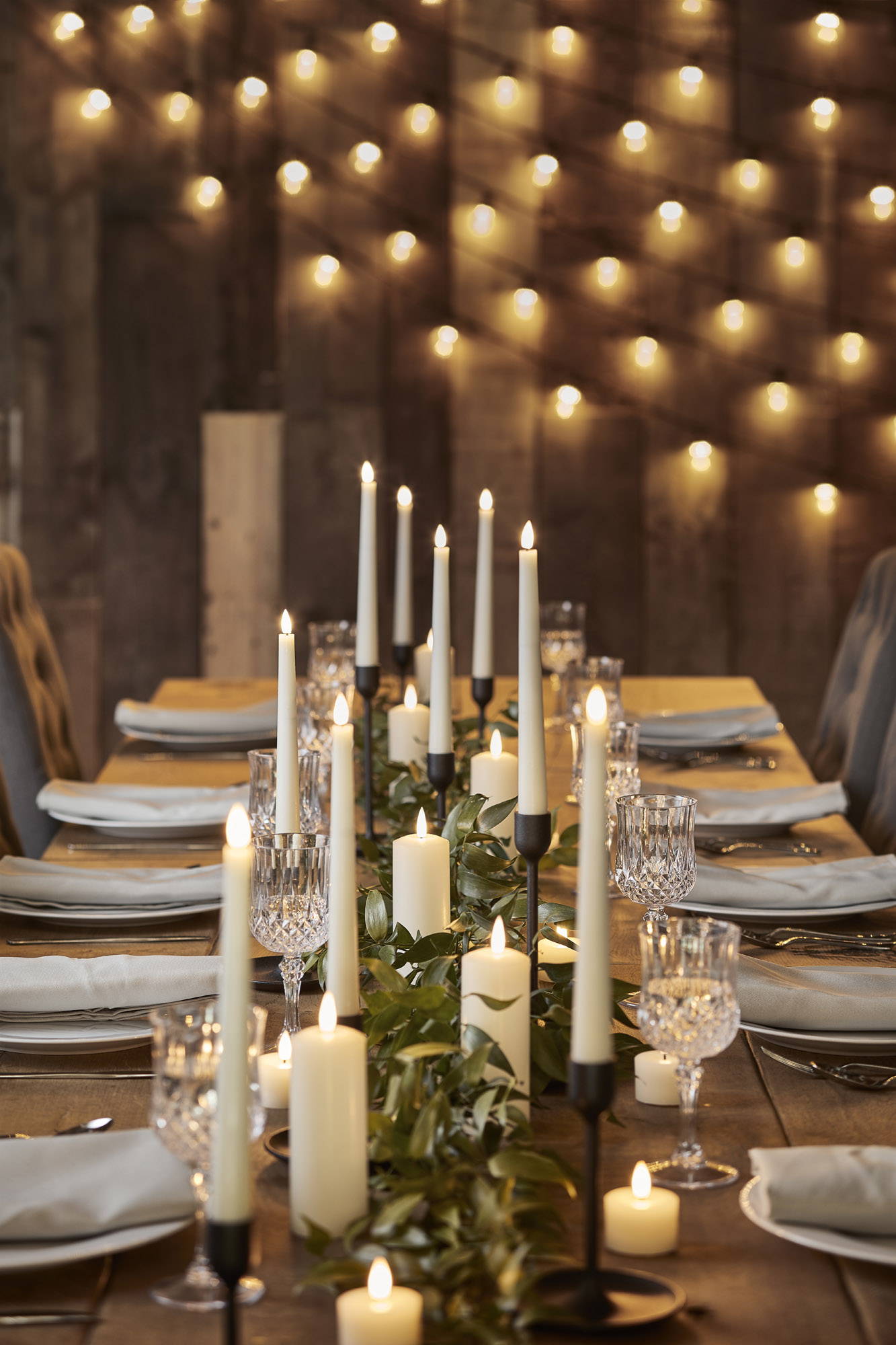 LED candles and taper candles on a dining table with festoons in the background.